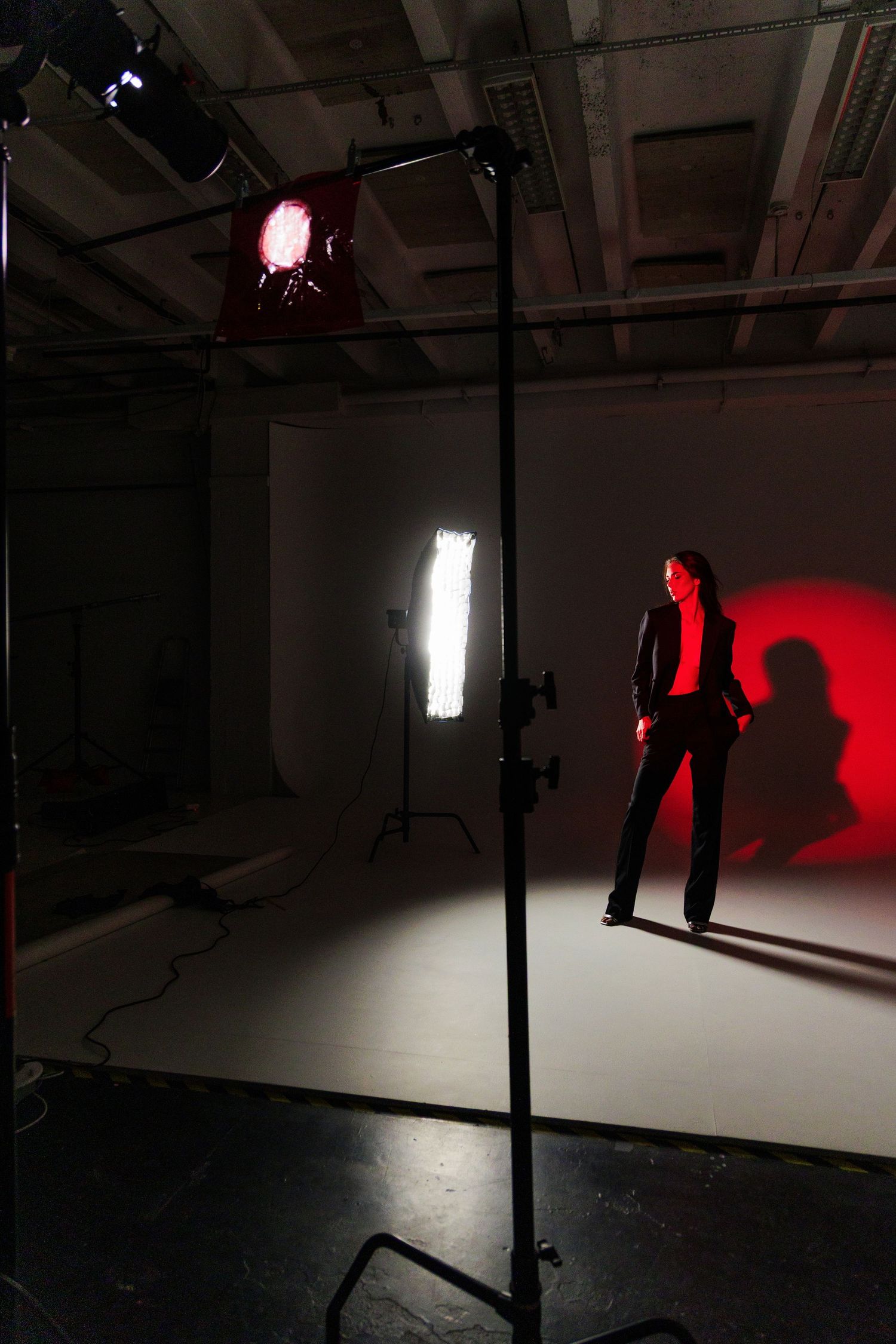 A model poses in a professional photo studio with dramatic red and white lighting against a white backdrop.