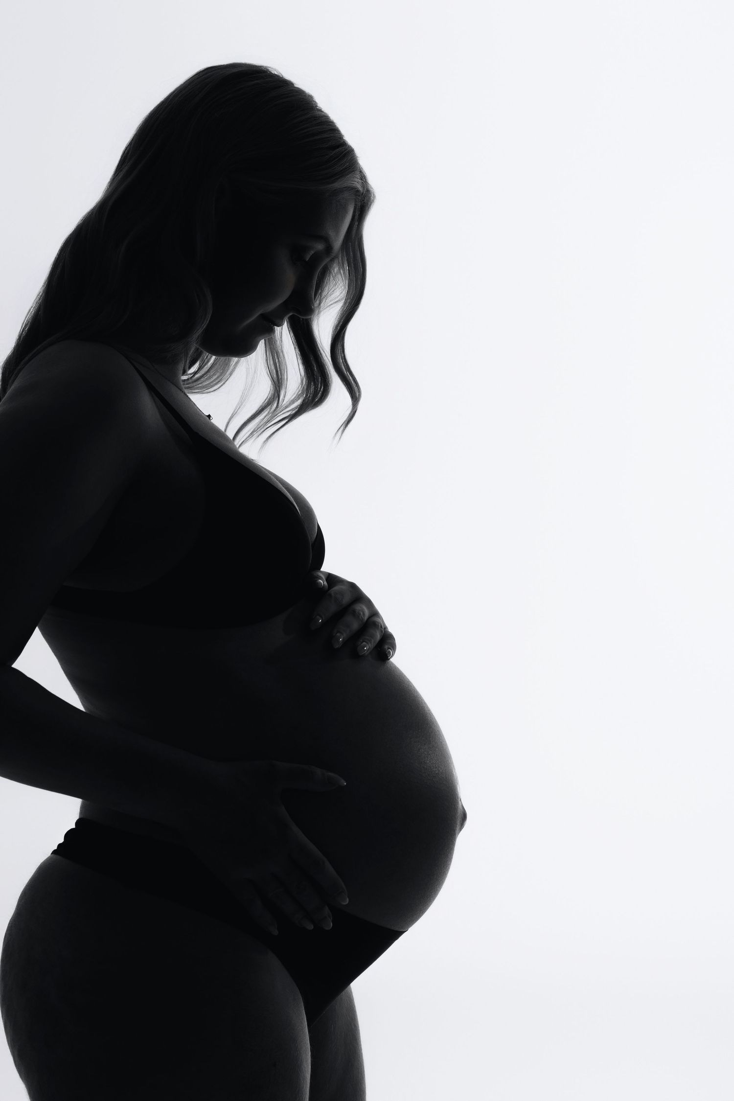 Silhouette of a pregnant woman cradling her baby bump against a white background.
