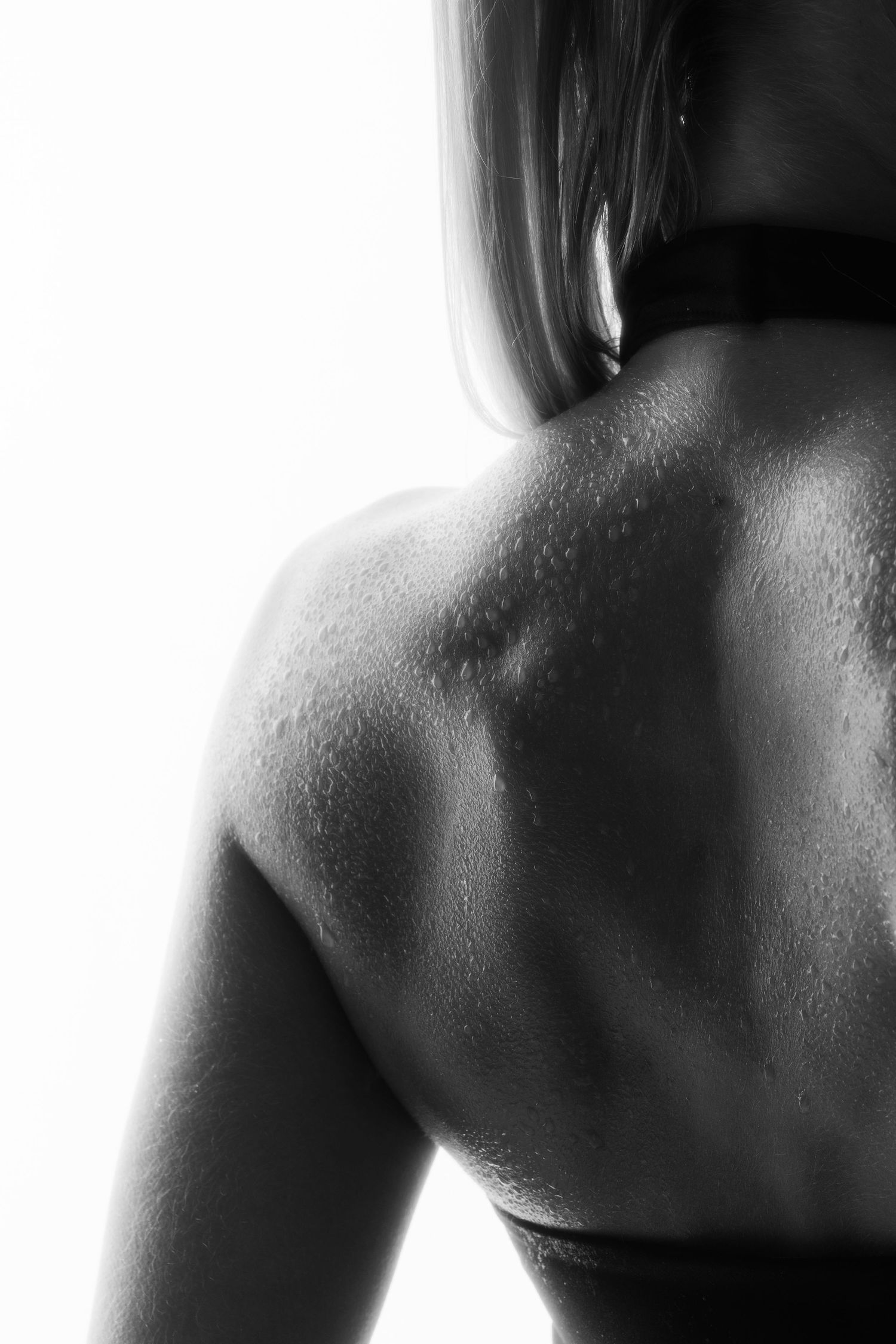 Black and white close-up of a woman's bare shoulder and back with water droplets.