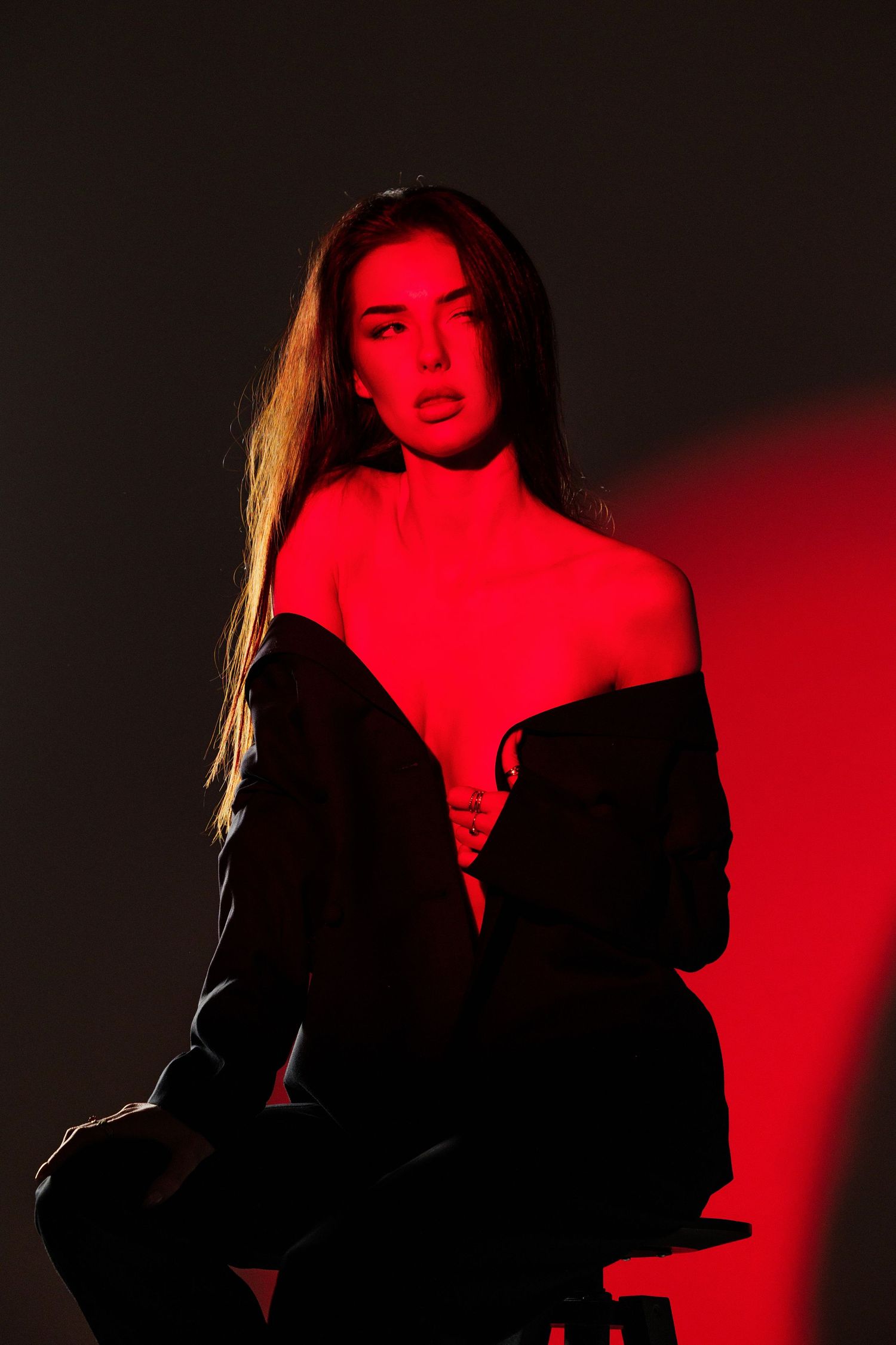 Woman posing dramatically in black outfit under red studio lighting against dark background.