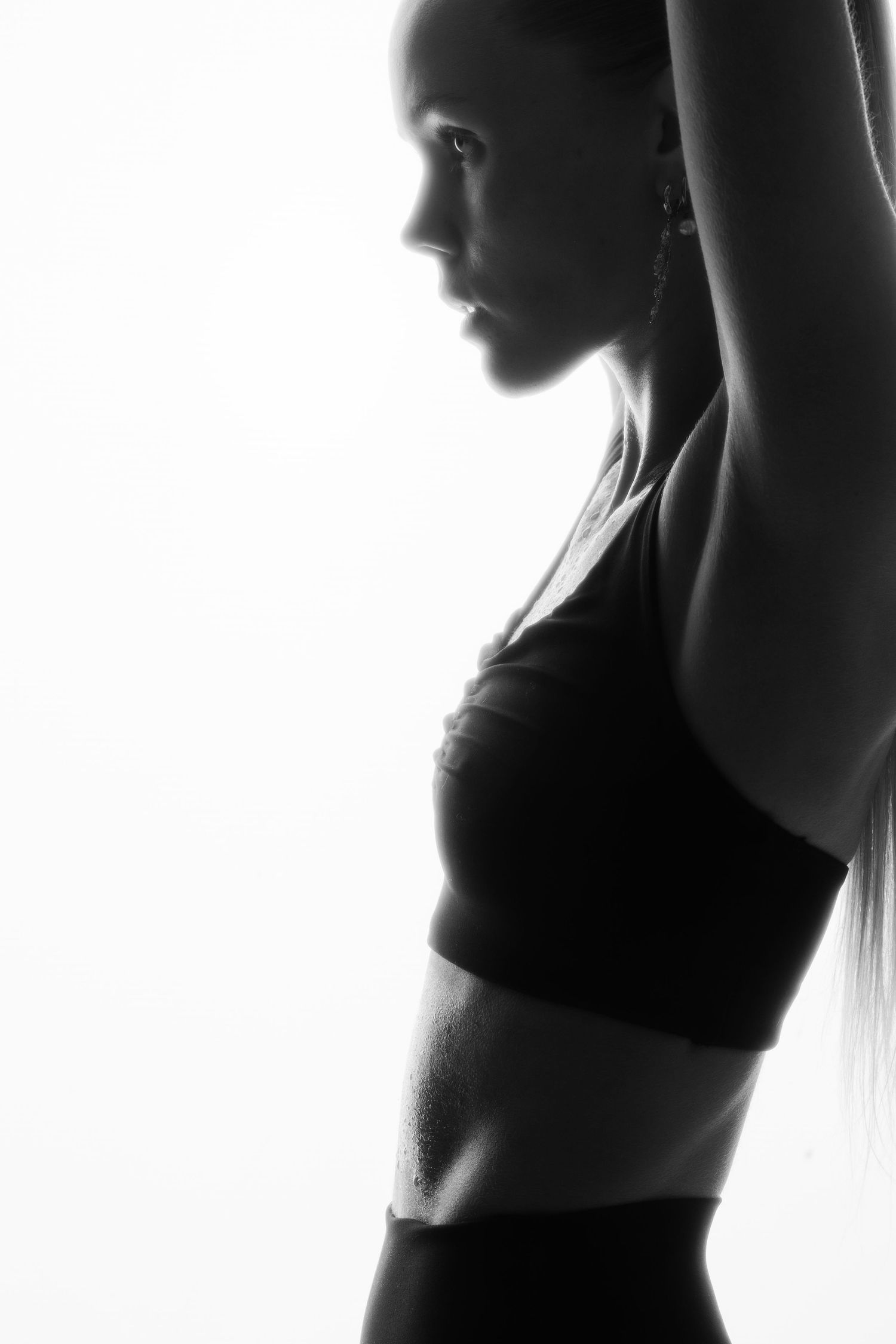 Black and white silhouette of a fit woman in sports bra stretching arms overhead.