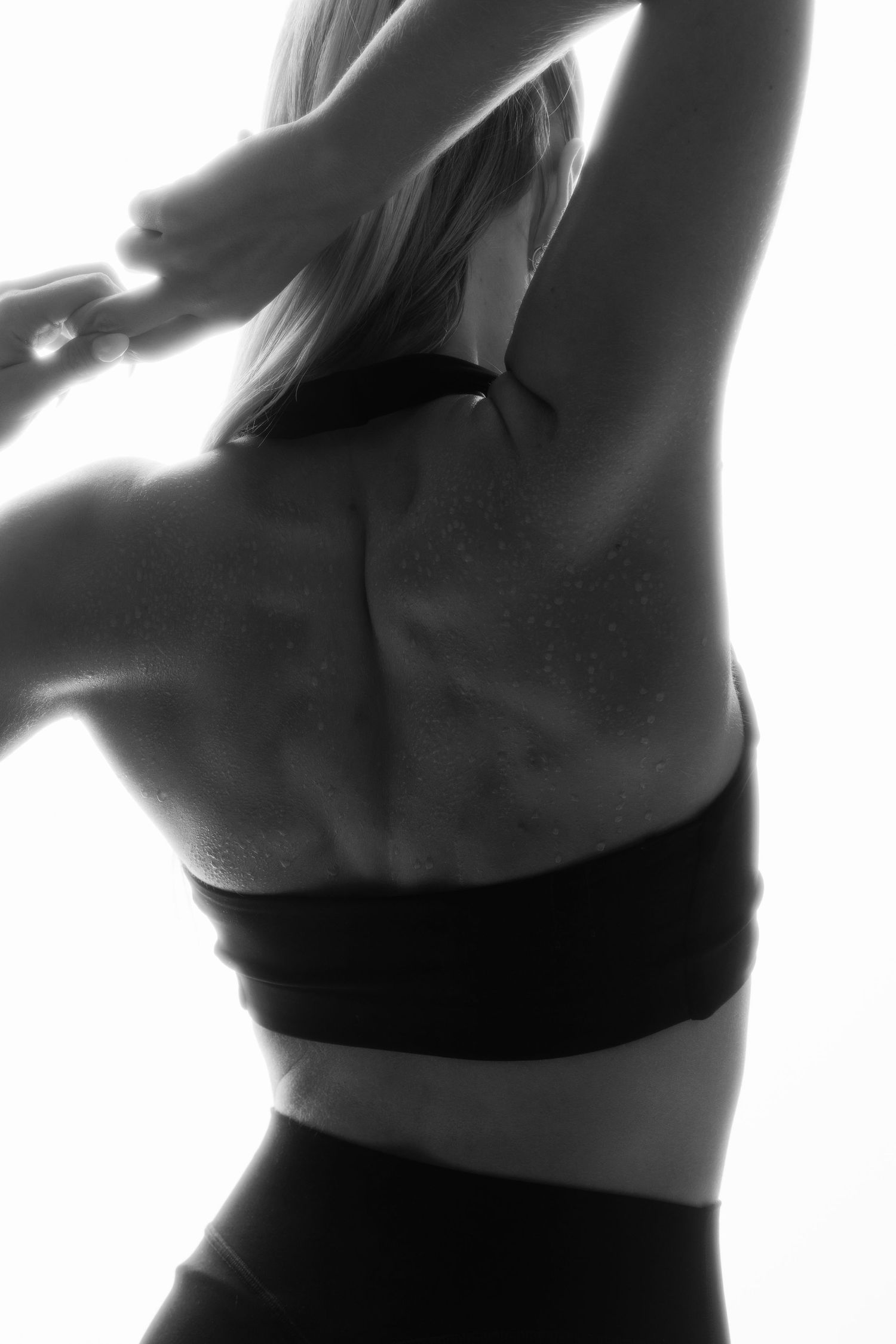 Black and white photo of a fit woman's back in a sports bra with arms raised.