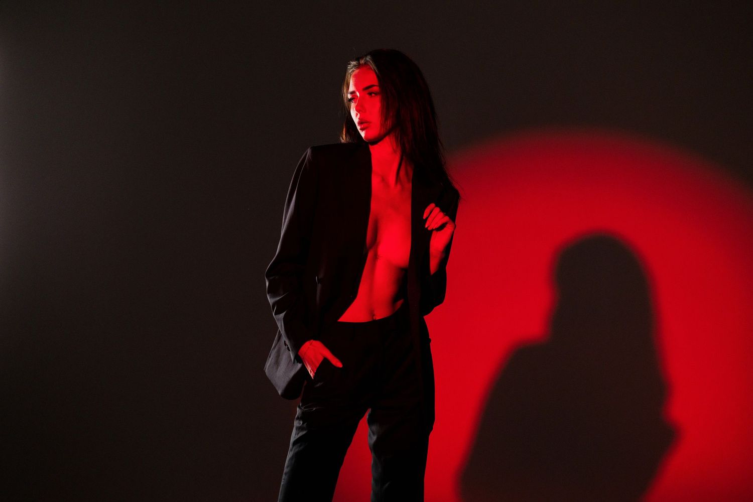 A stylish person in a black blazer poses against a dark background with a dramatic red circular light.
