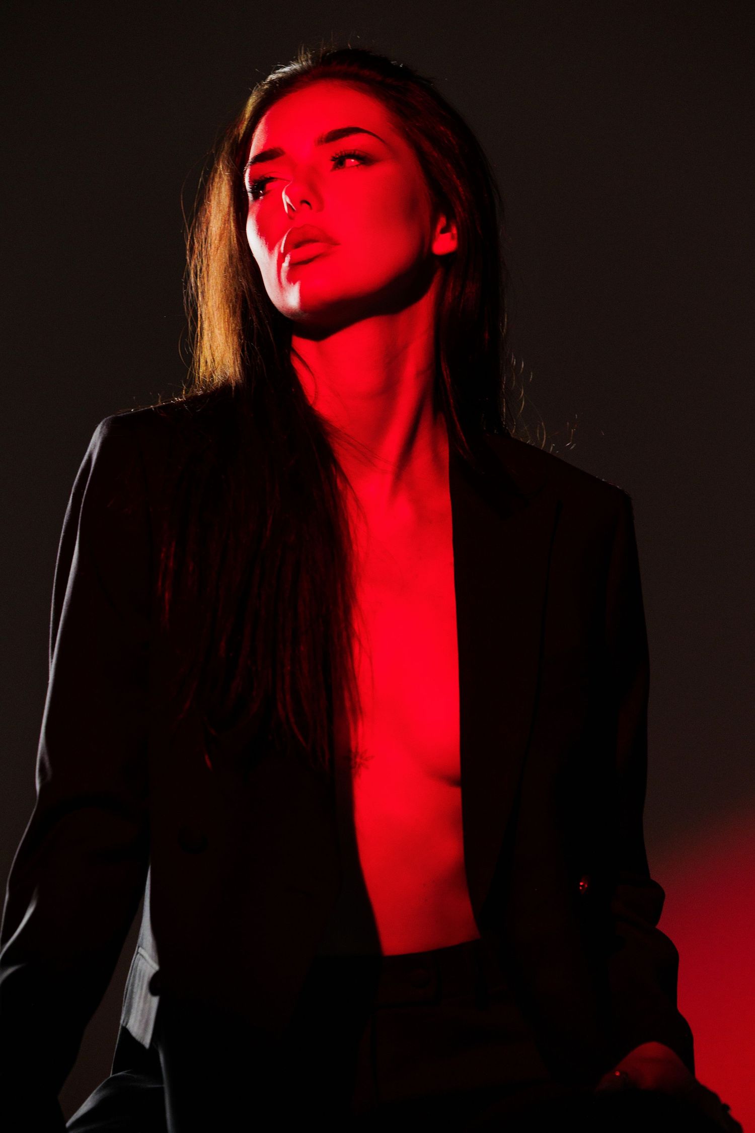 A woman in a black blazer poses dramatically under striking red lighting against a dark background.