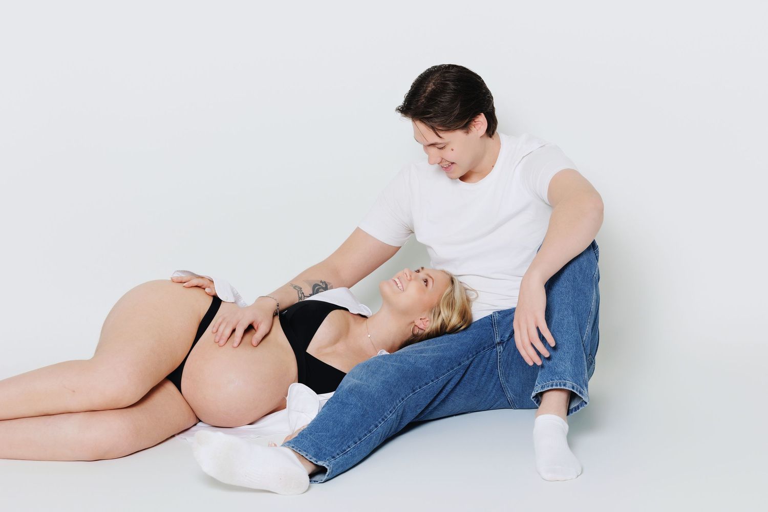 Couple relaxing on the floor during a maternity photoshoot, man gazing at pregnant partner.