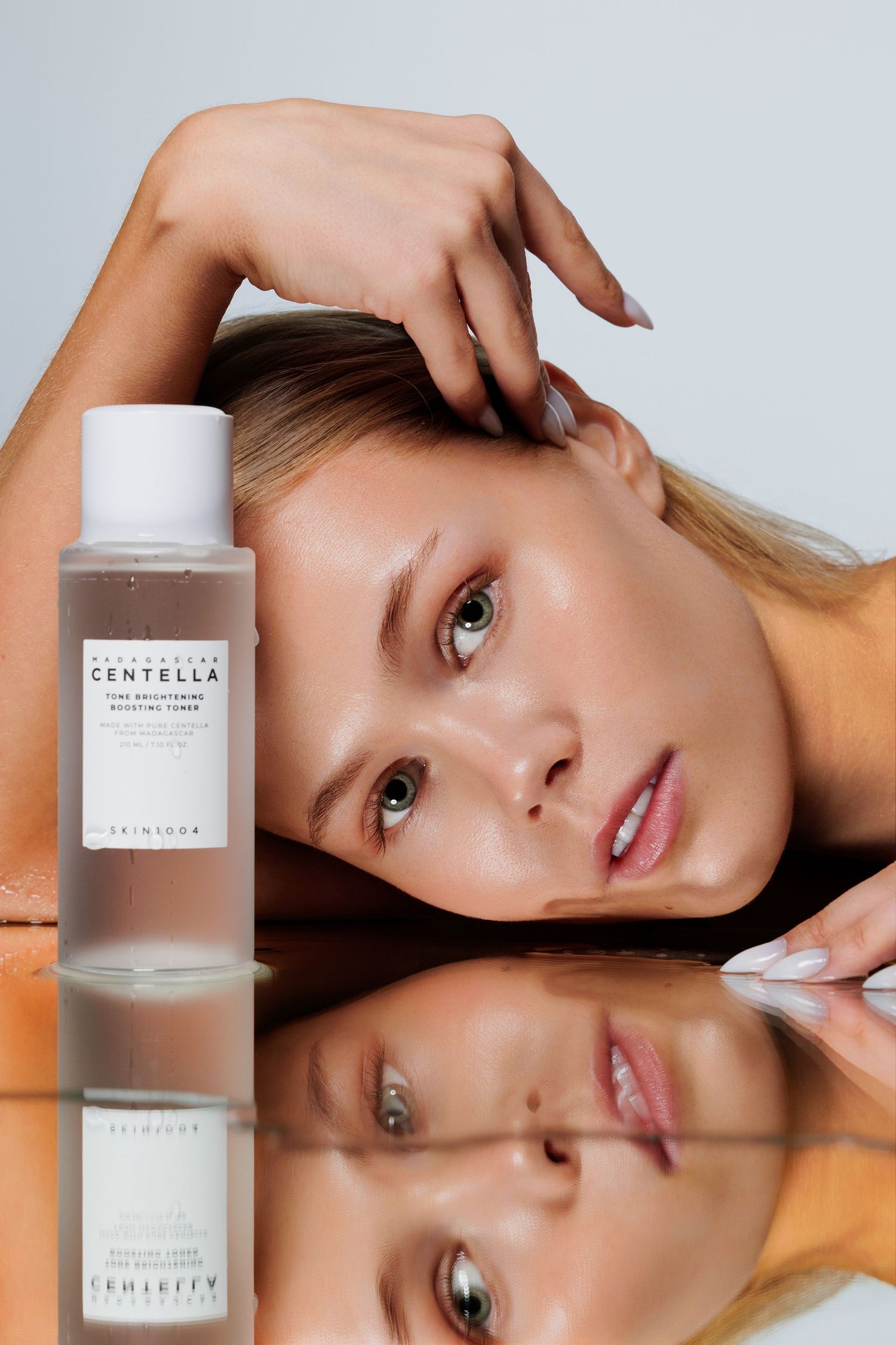 Close-up of blonde model posing with Skinsider Centella toner on mirrored surface.