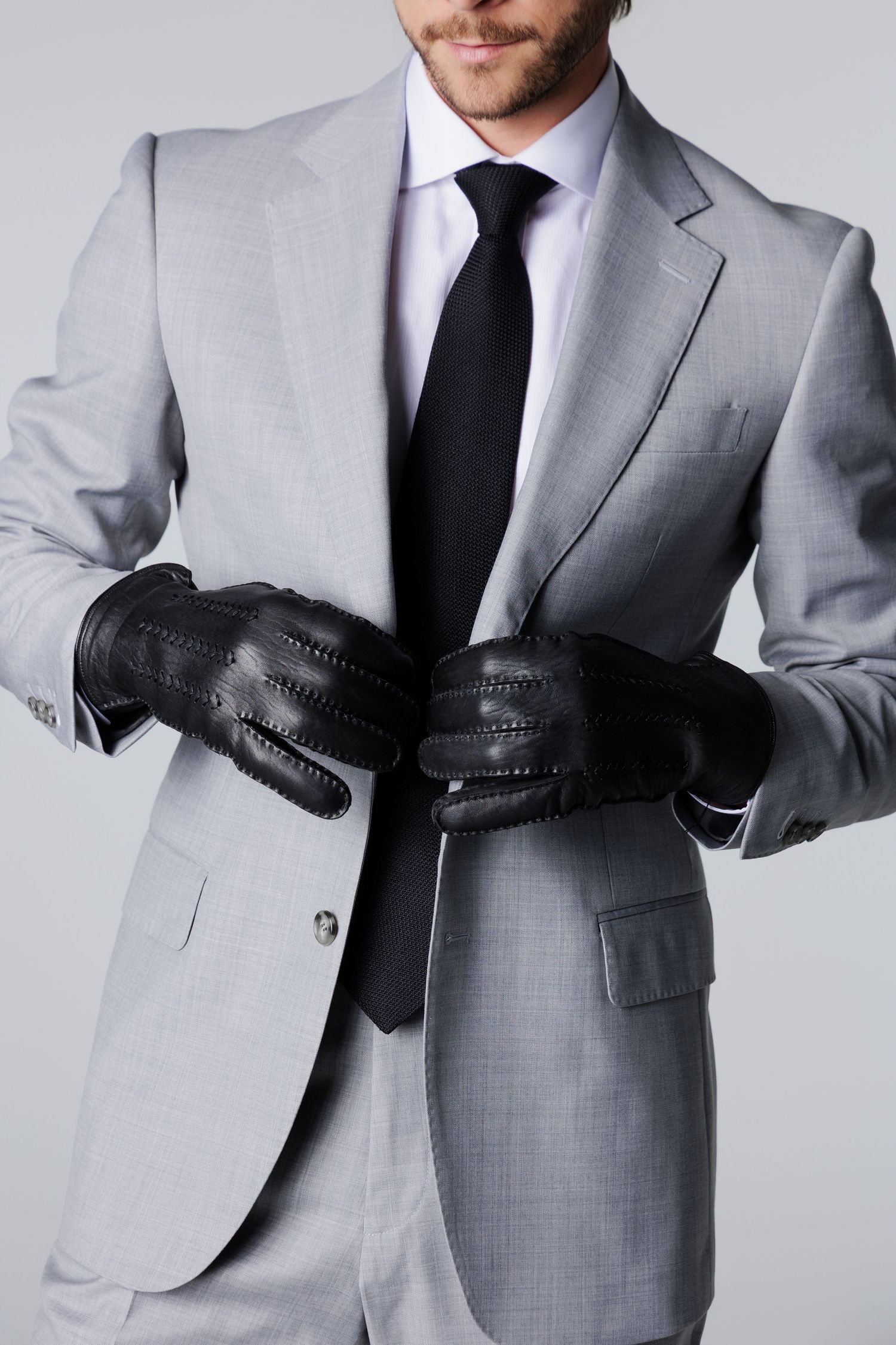Close-up of man in gray suit adjusting black leather gloves with dark tie.