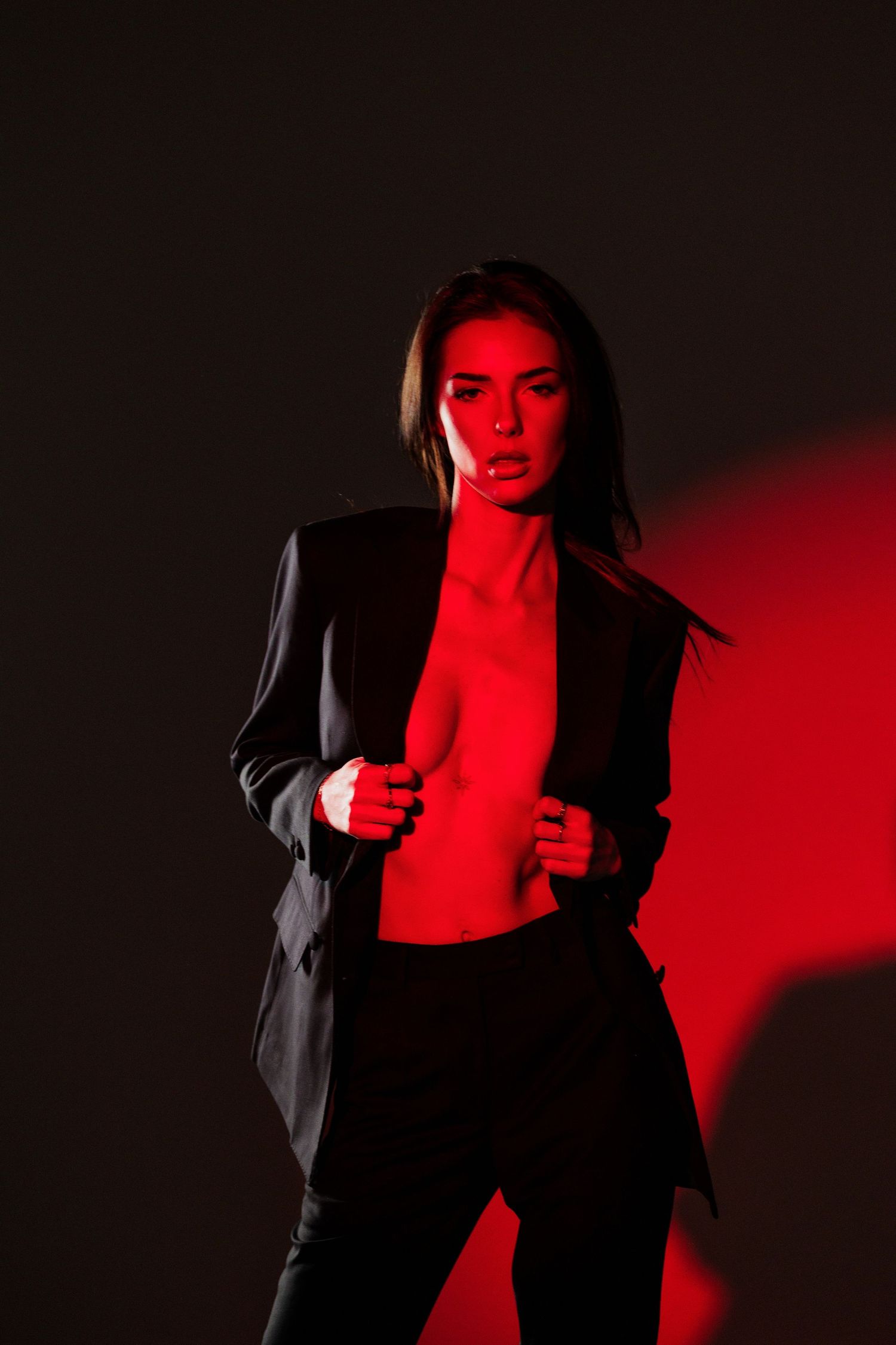 Woman in black blazer posed dramatically under red lighting on dark background.