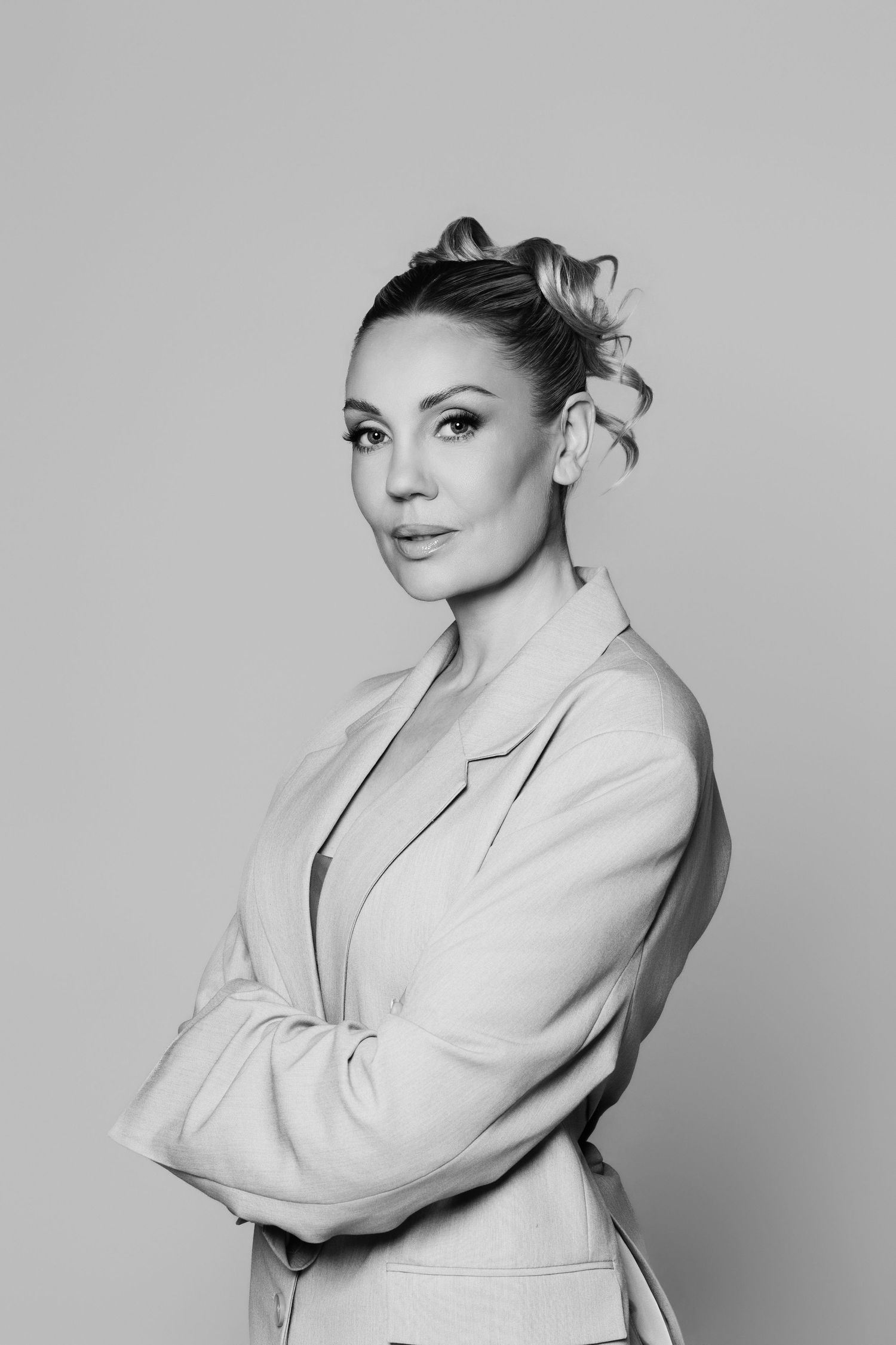 Black and white portrait of a confident woman in a blazer with arms crossed and elegant updo hairstyle.