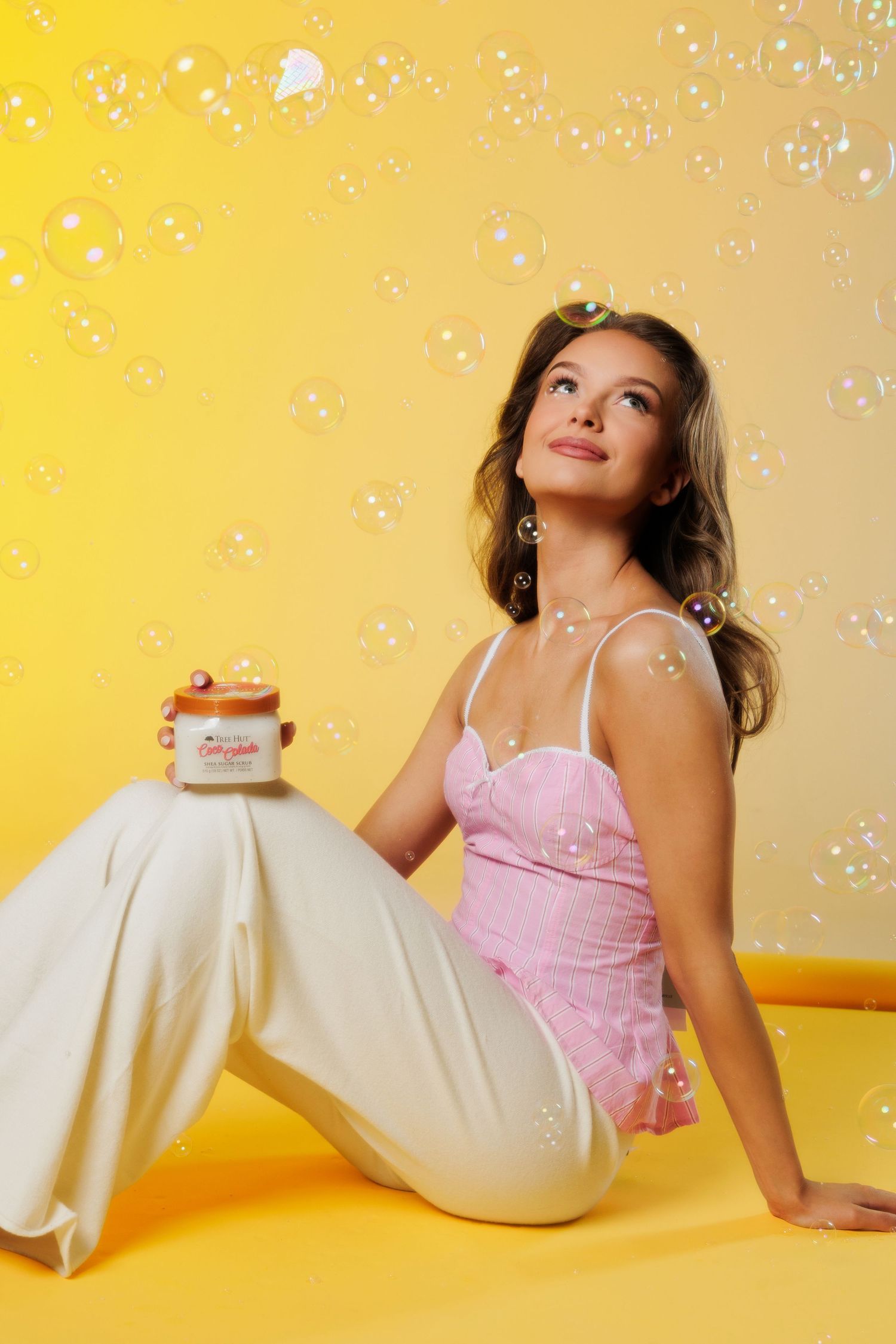 Woman in pink corset top sitting on yellow floor surrounded by floating soap bubbles.