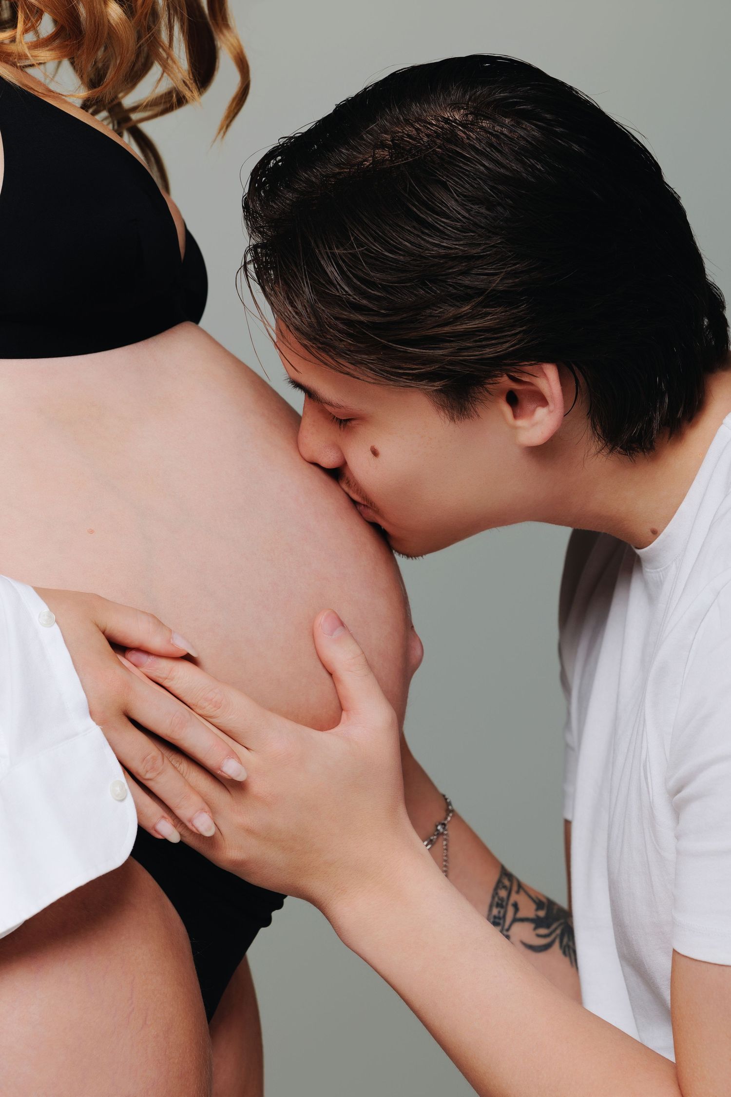 Partner tenderly kissing pregnant woman's baby bump in an intimate maternity photo.