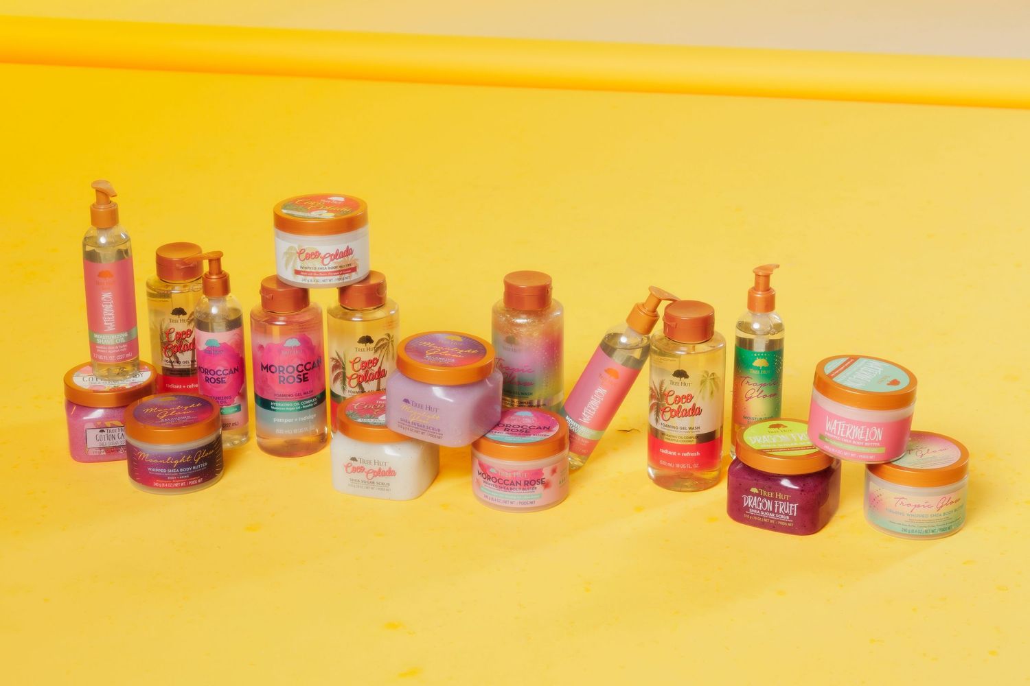 Collection of pink and gold beauty and hair care products arranged on yellow surface.