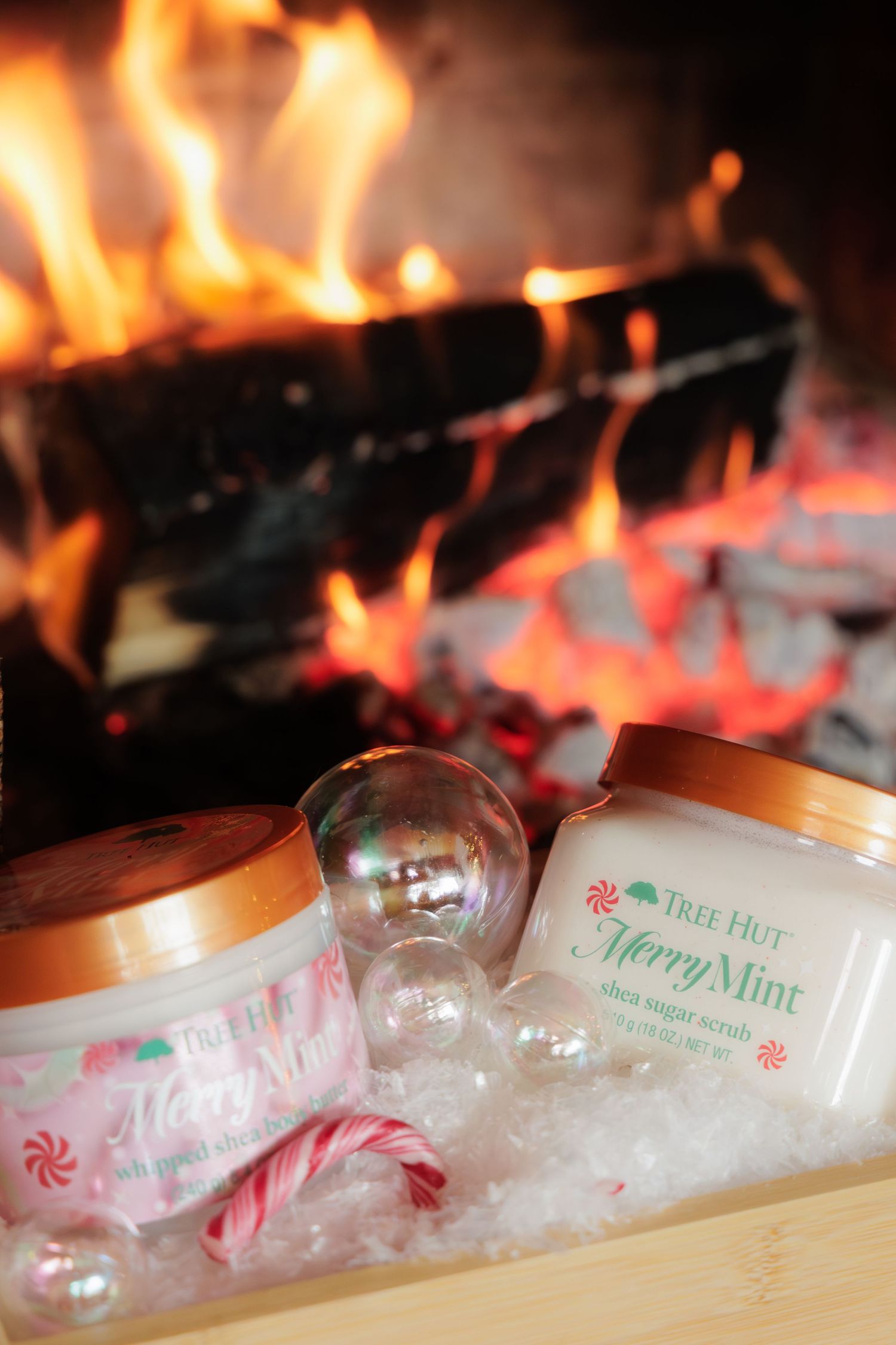 Tree Hut Merry Mint shea sugar scrub jars displayed with candy canes near a fireplace.