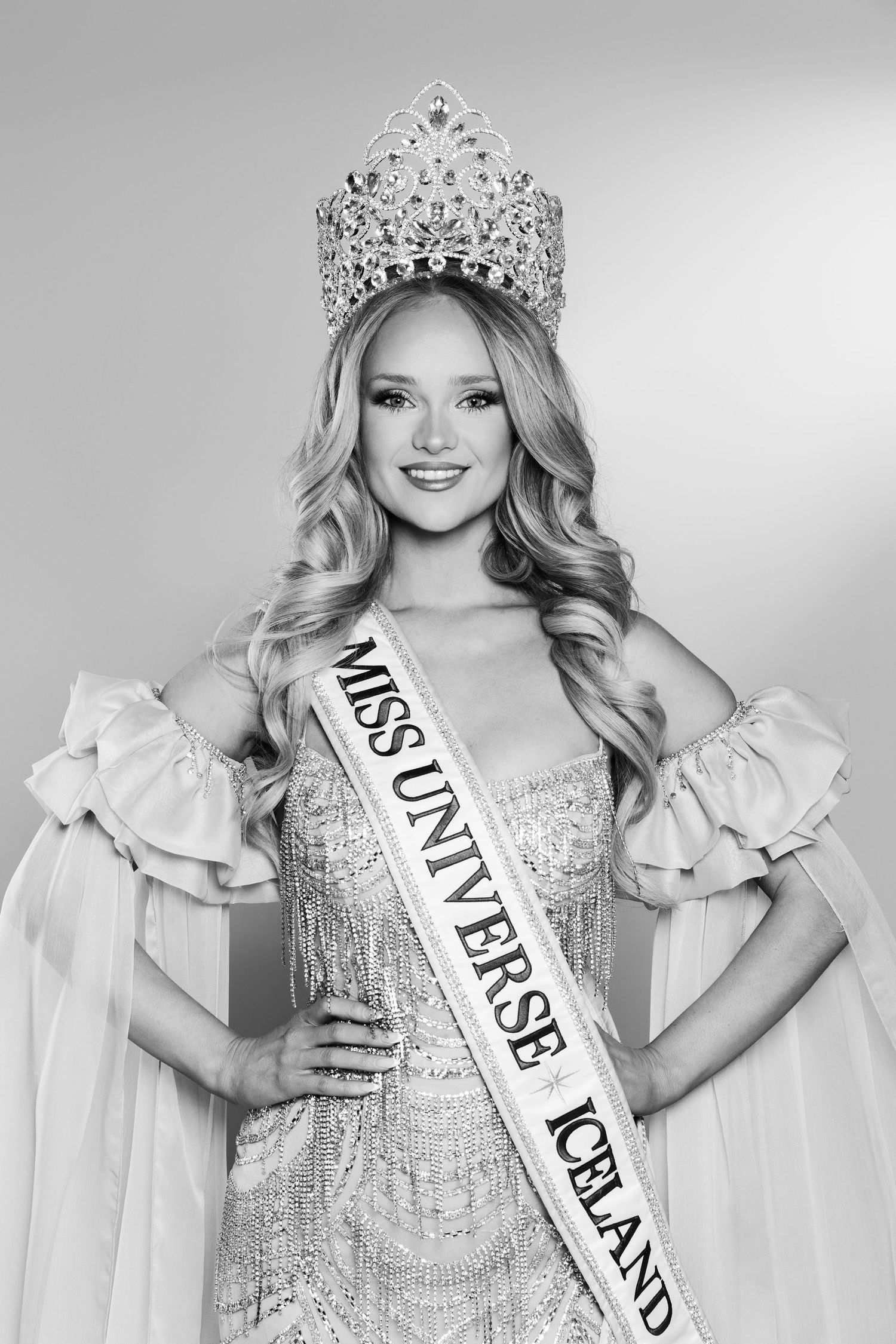 Black and white portrait of Miss Universe Iceland contestant wearing crown and sash in elegant gown.