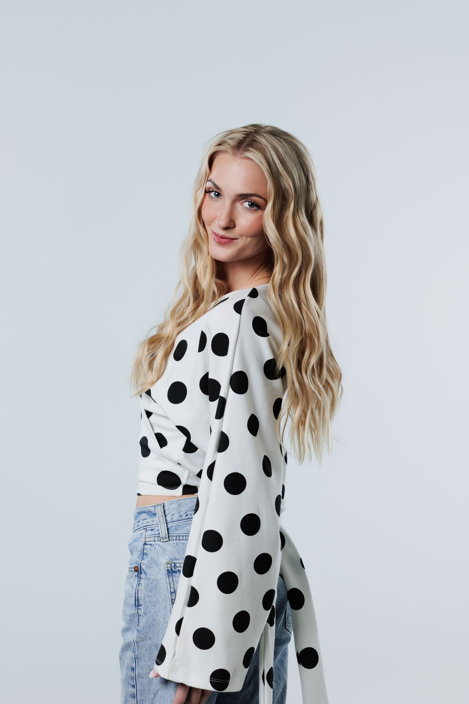 Blonde woman in polka dot top and jeans posing in studio.