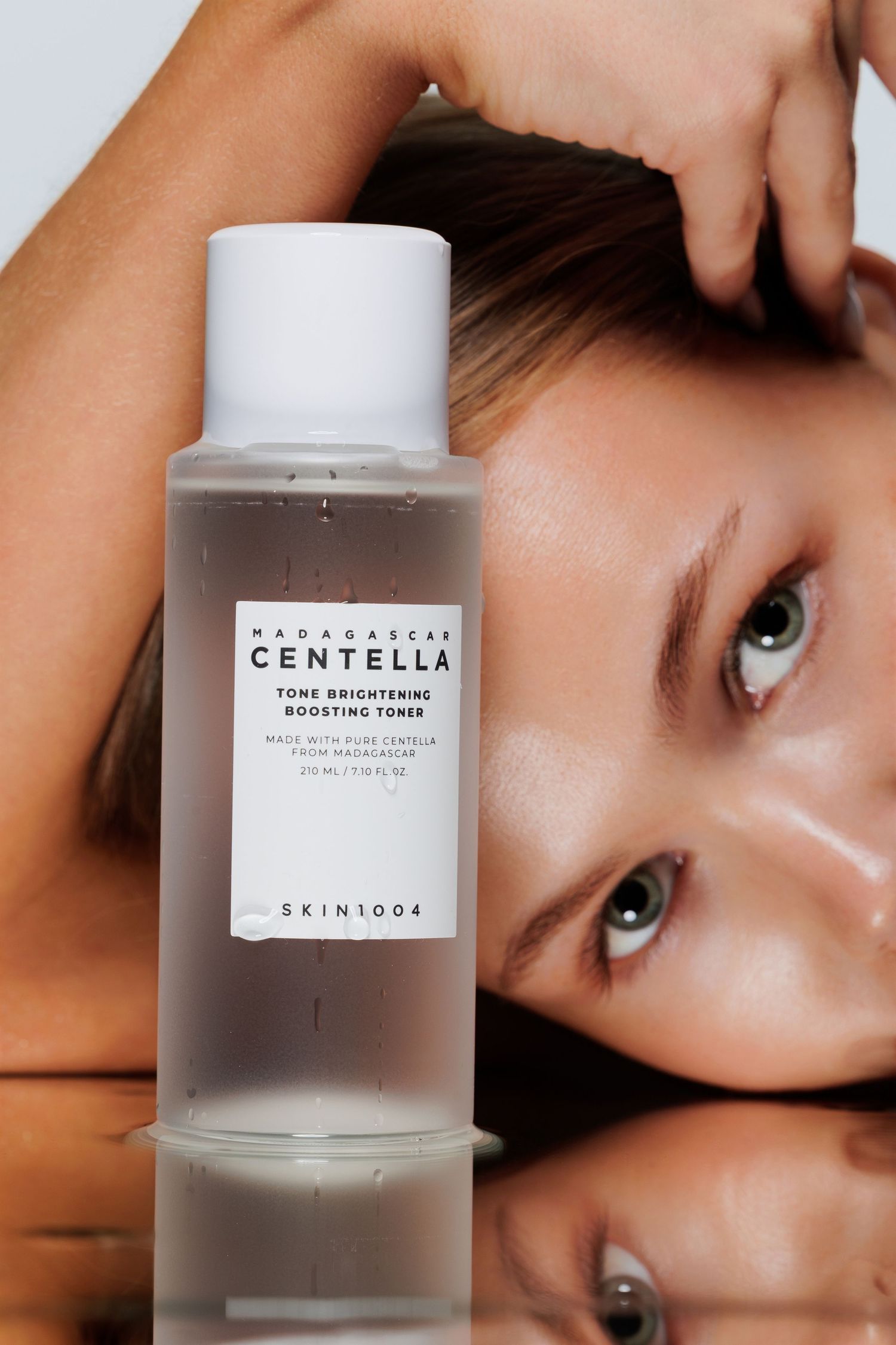 SKIN1004 Madagascar Centella Tone Brightening Boosting Toner bottle with a woman's reflection on a mirrored surface.