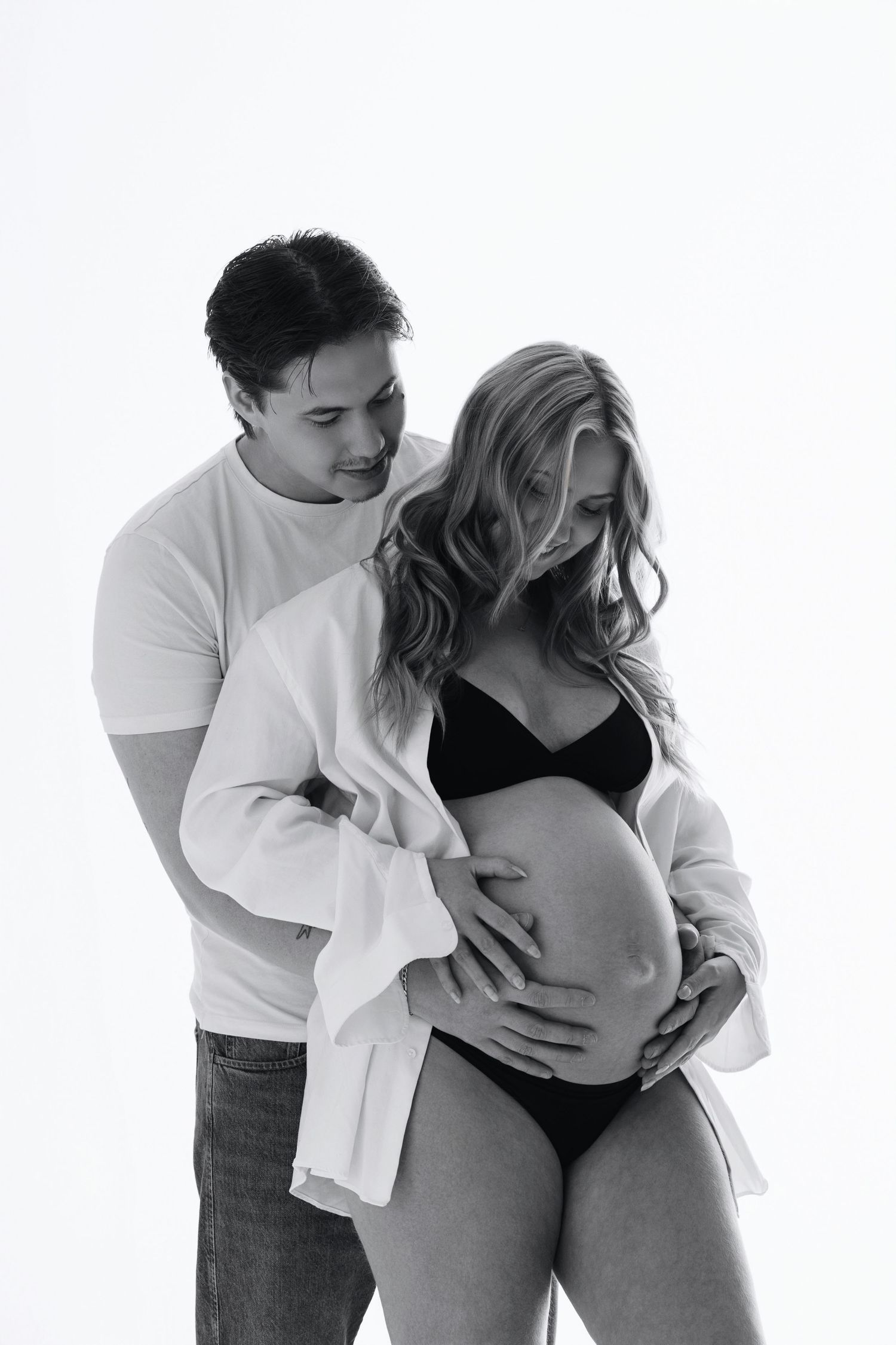 Black and white maternity photo of couple embracing, man wrapping arms around pregnant woman.