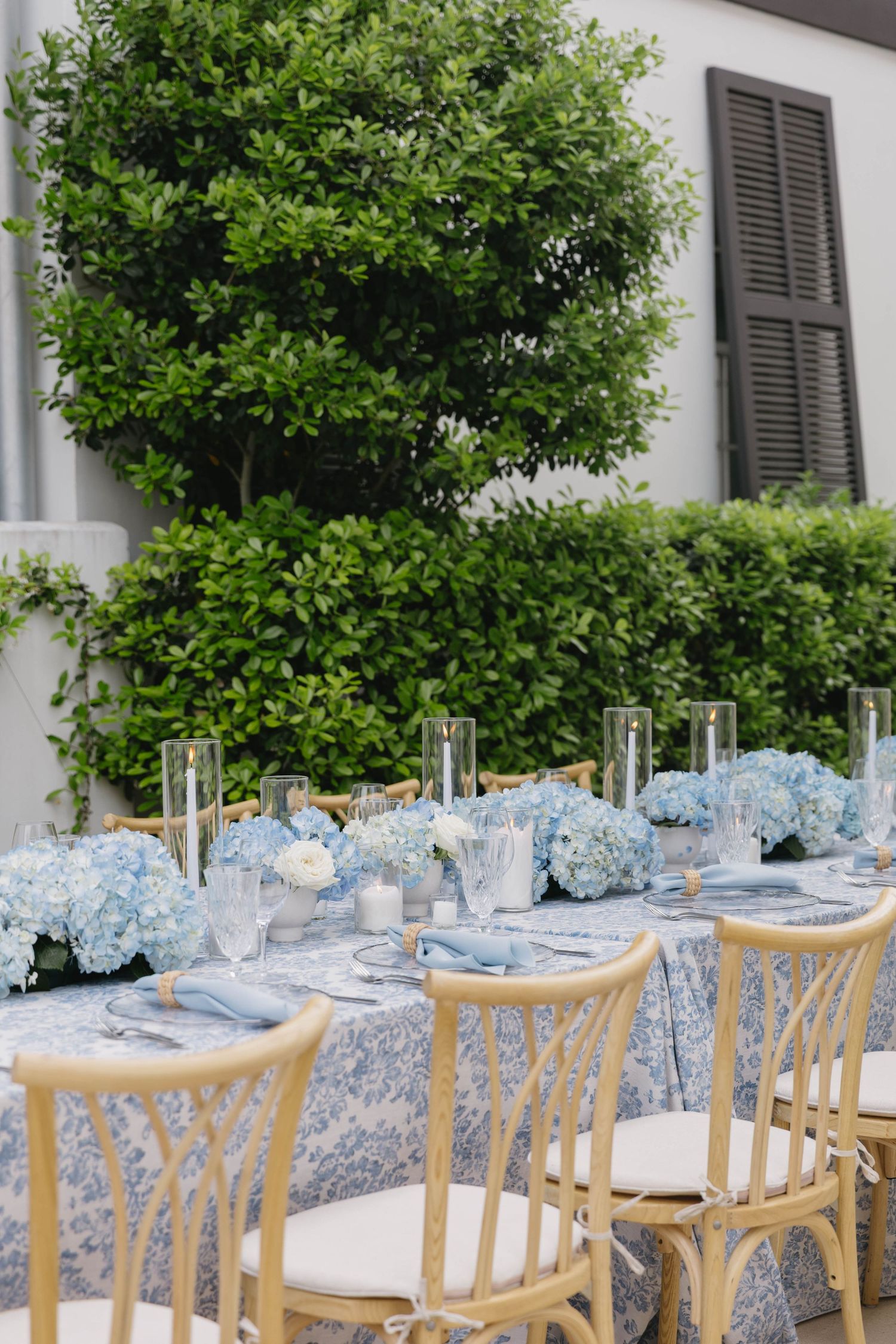 Outdoor wedding reception table with blue hydrangeas, blue toile linens, and gold chiavari chairs.