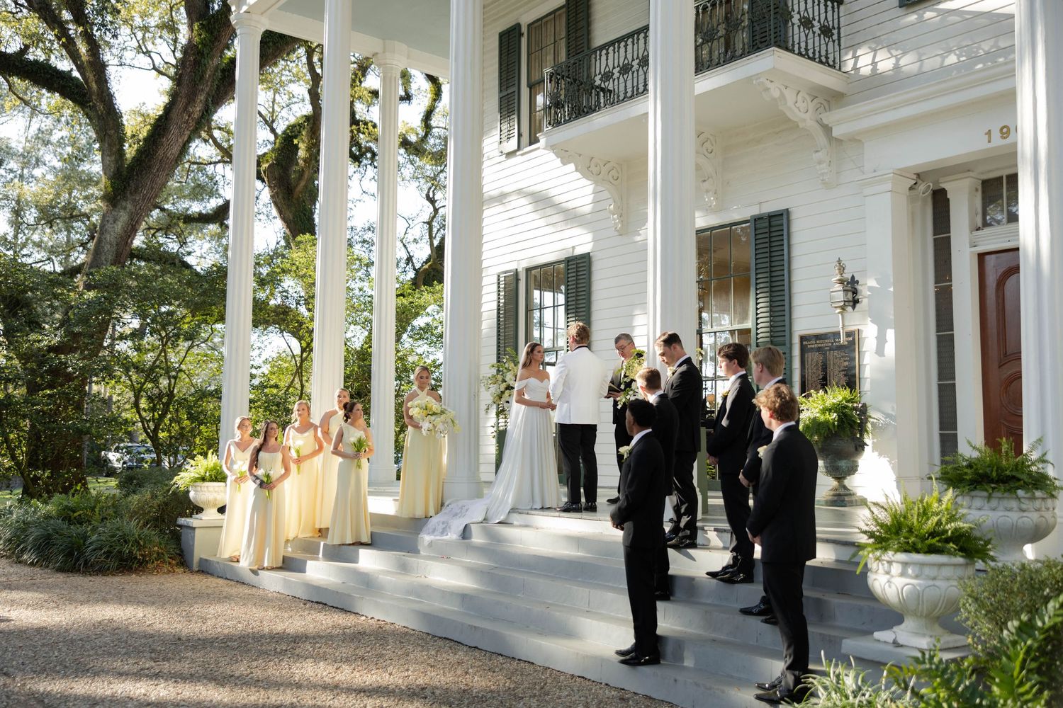 Wedding ceremony on the grand steps of a white Southern mansion with bridesmaids in yellow dresses and groomsmen.