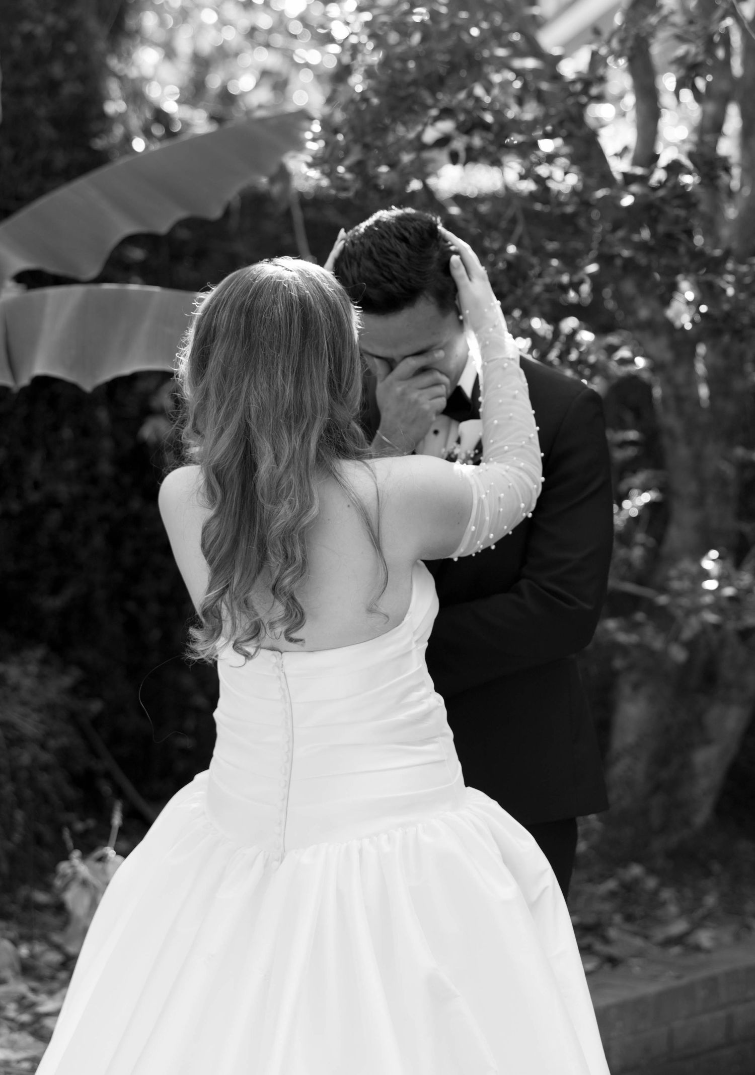 Emotional black and white photo of groom covering face with hands during heartfelt first look with bride.