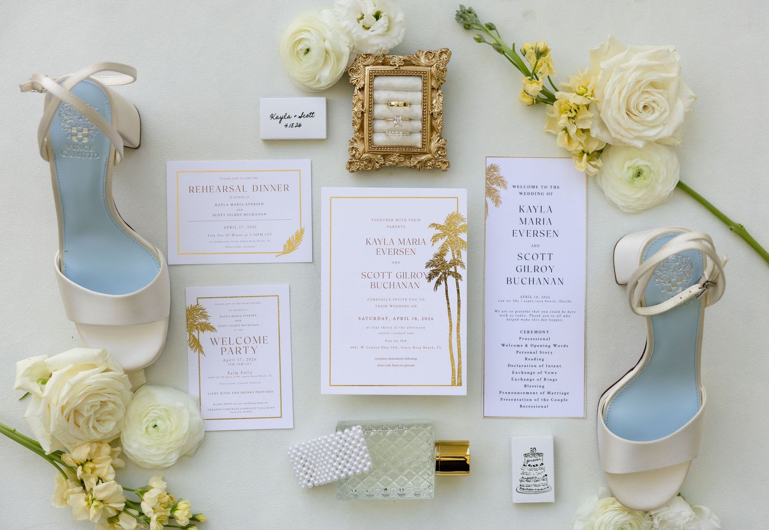 Elegant wedding invitation suite with gold palm tree design, white heels, and white floral arrangements.