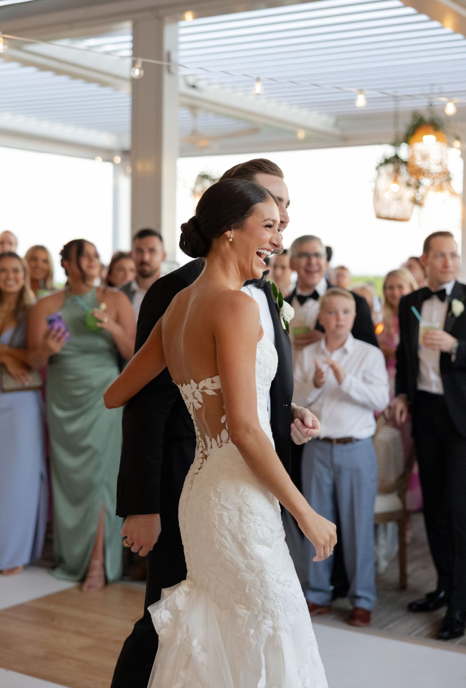 Bride in lace backless wedding gown laughs with groom during wedding reception entrance before guests.
