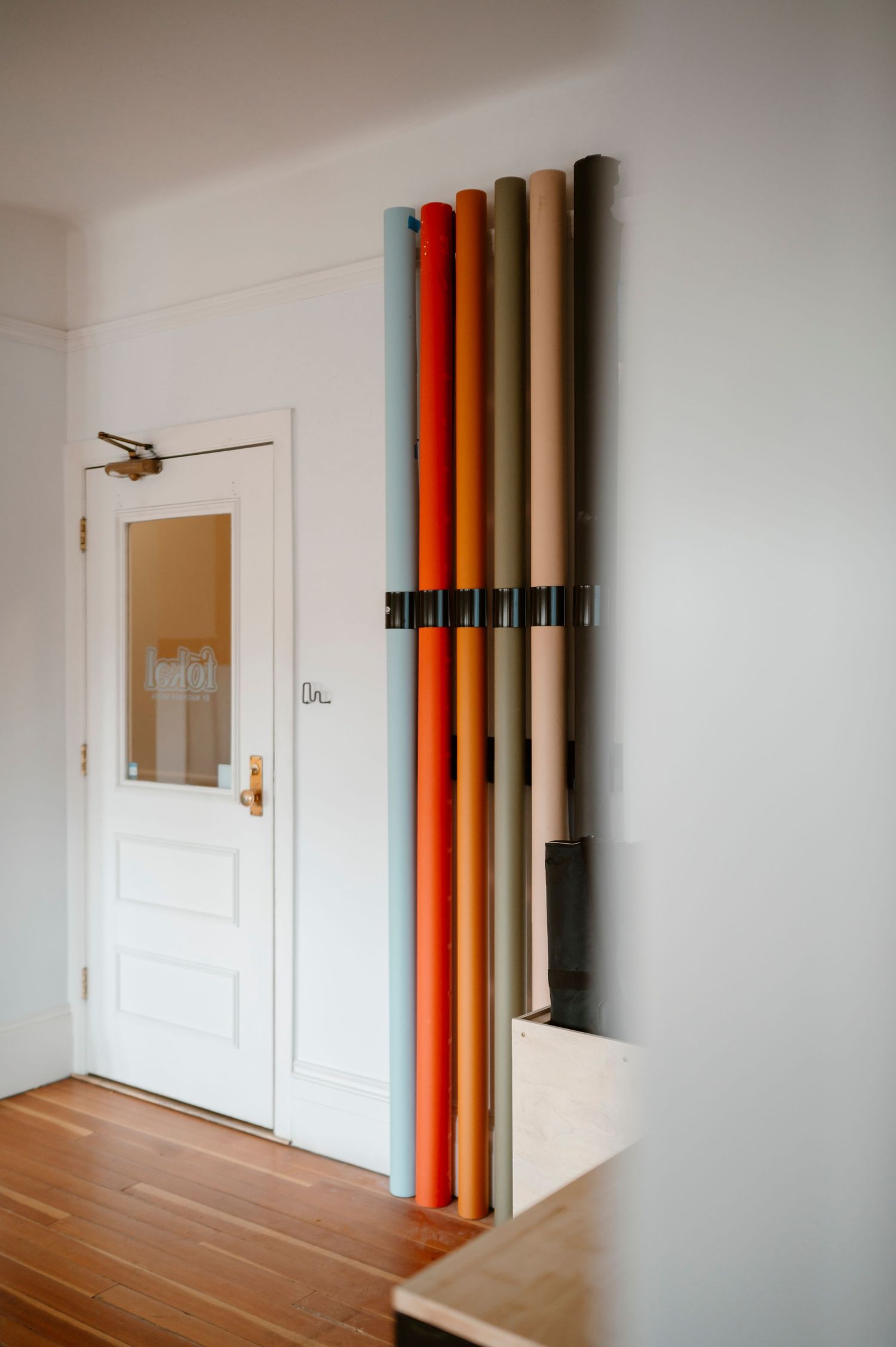 Interior design featuring colorful vertical tubes mounted on white wall near doorway.
