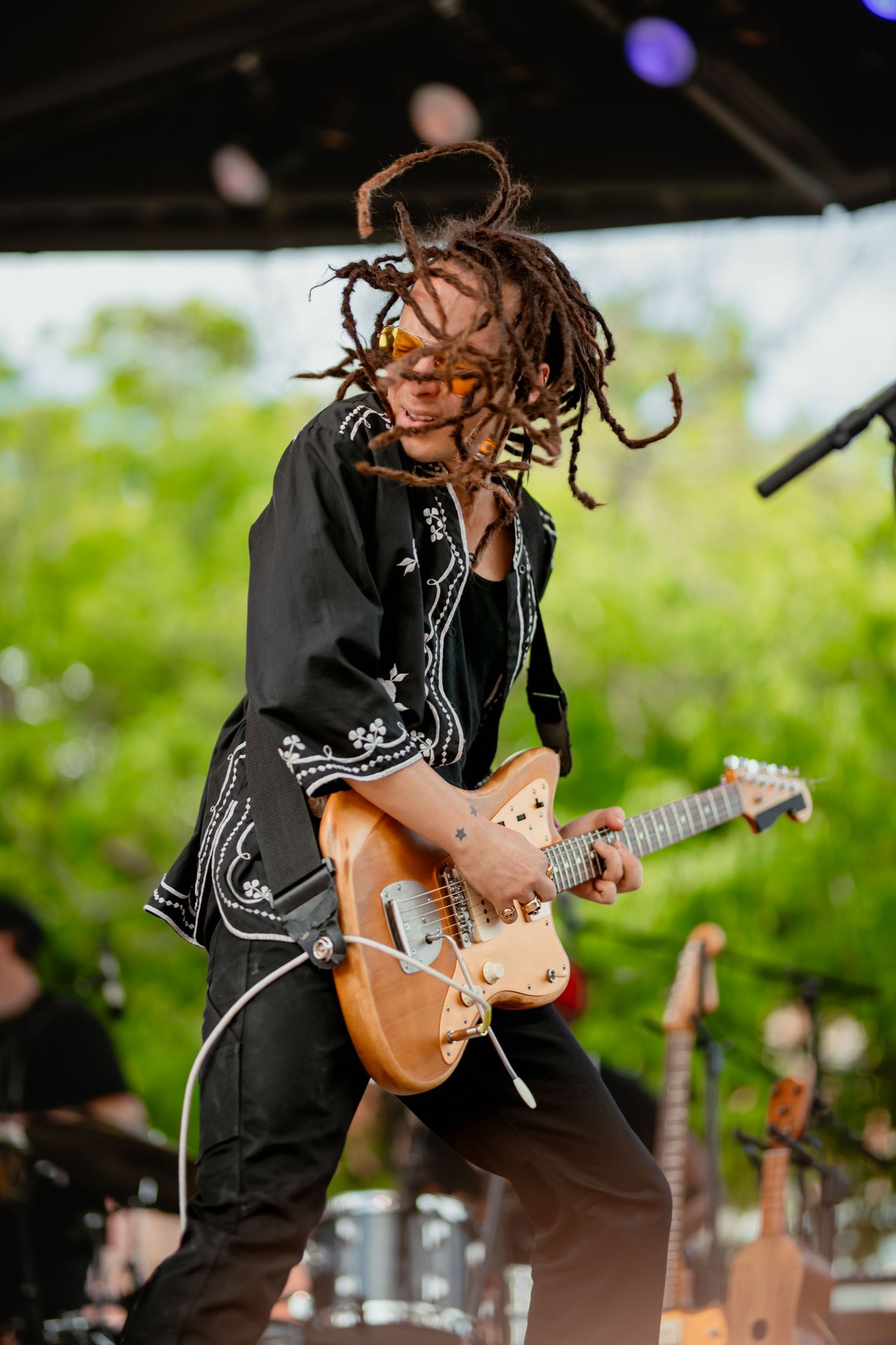 Musician performs energetically on stage with an electric guitar while dreadlocks fly through the air during performance.