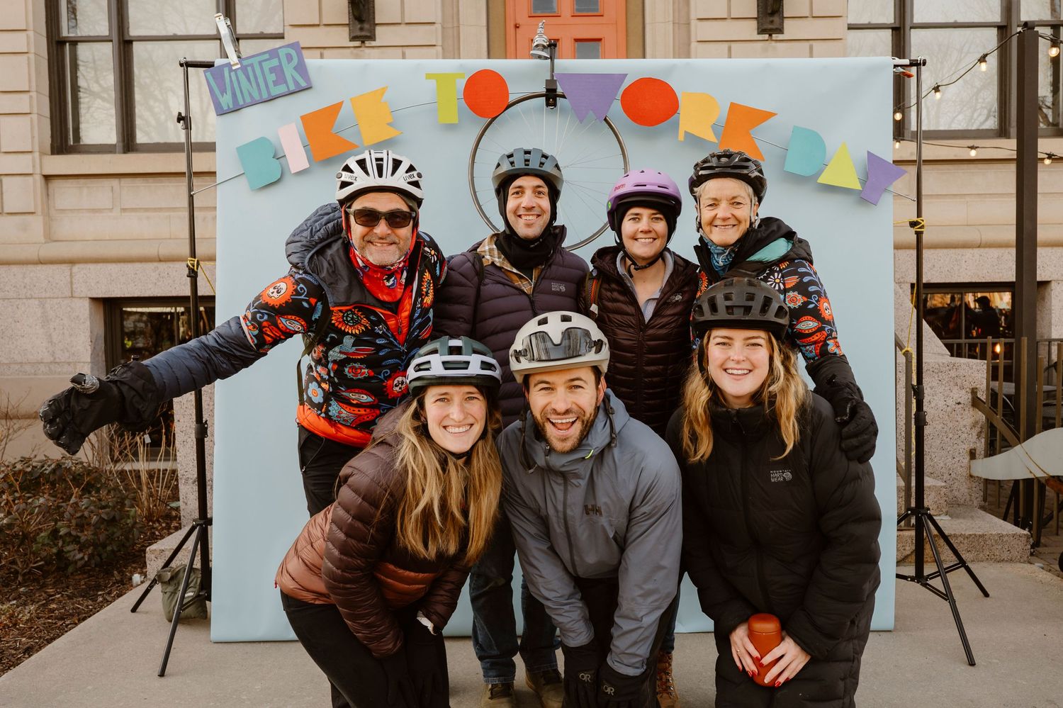 A group of cyclists in winter gear smiling together during a cold weather bike ride outdoors.