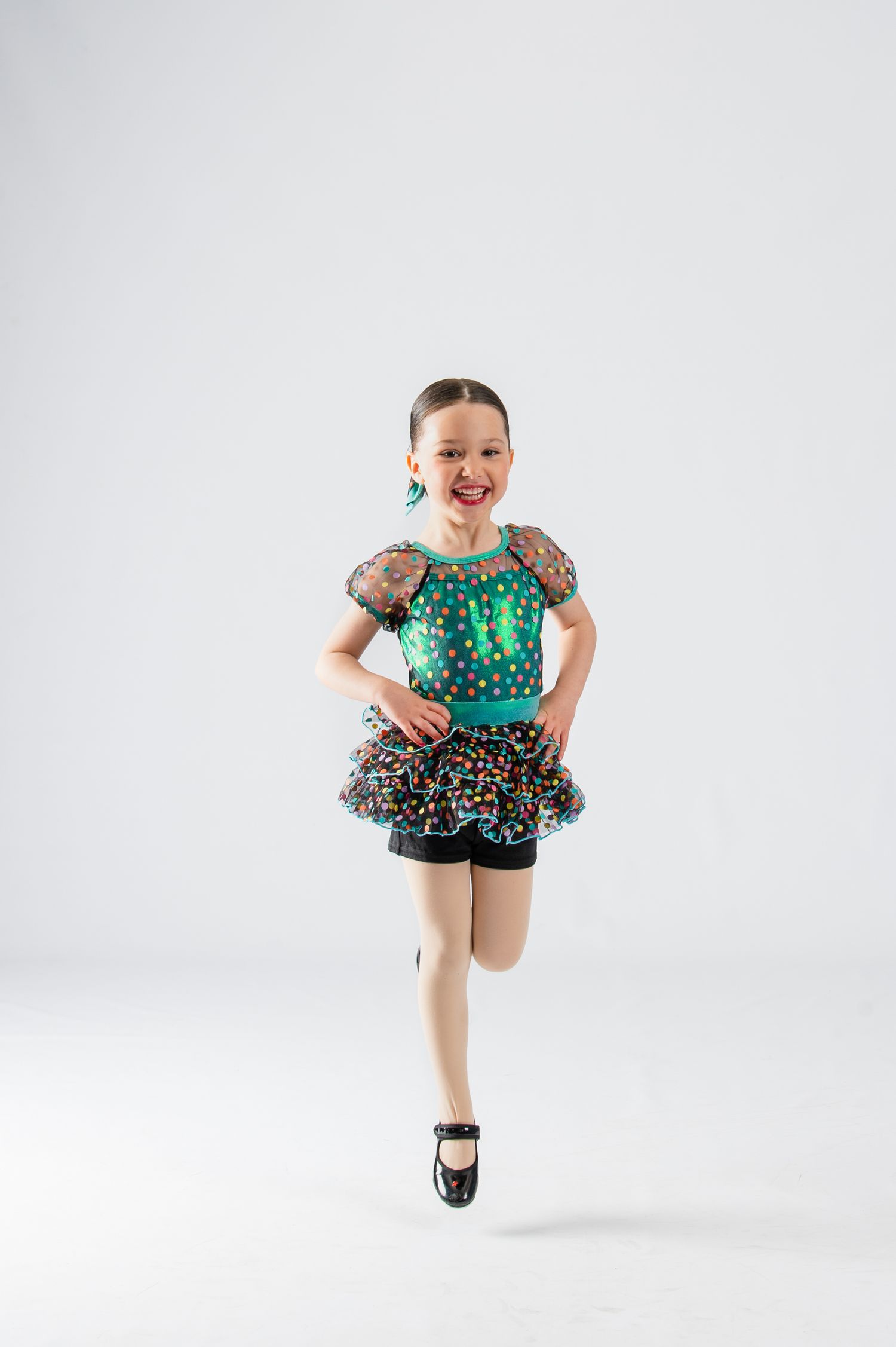 Dancer in green polka dot costume performing energetic jump with joyful expression.