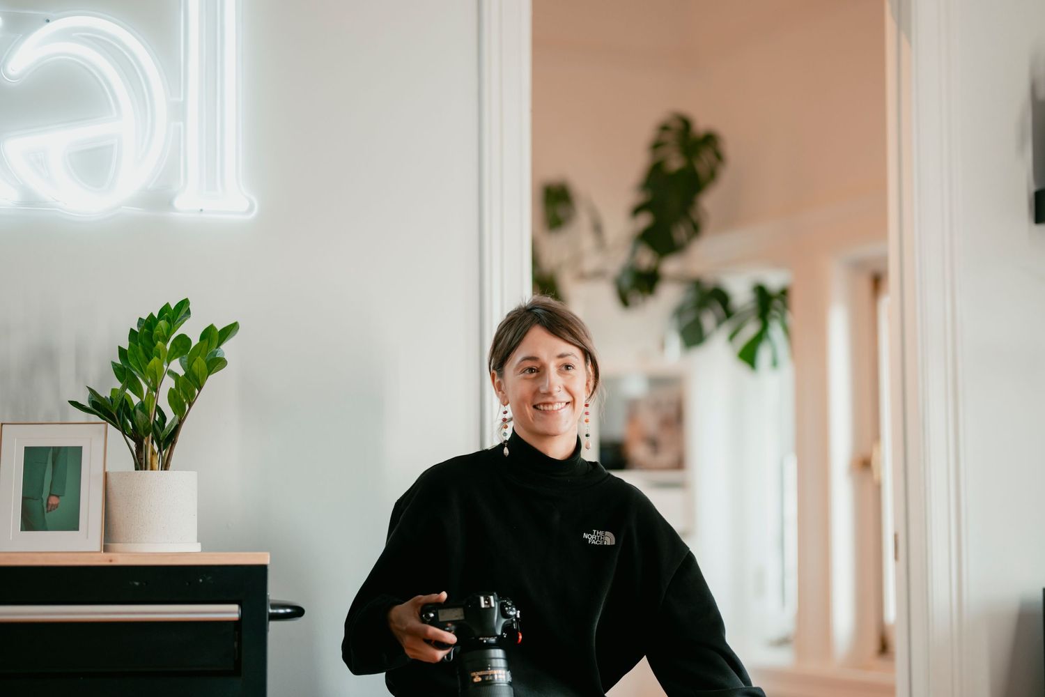 Portrait of a photographer in a black sweater holding a camera in a modern studio space.