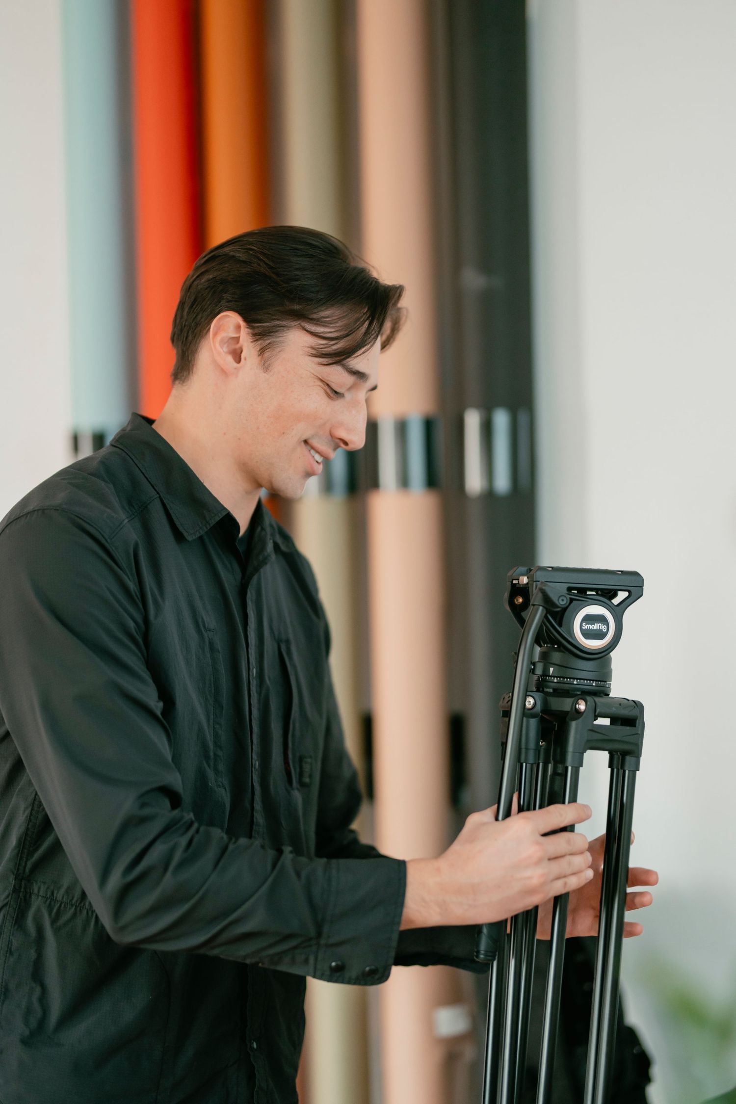 Photographer adjusting camera equipment on a tripod in a studio with colorful wall panels.
