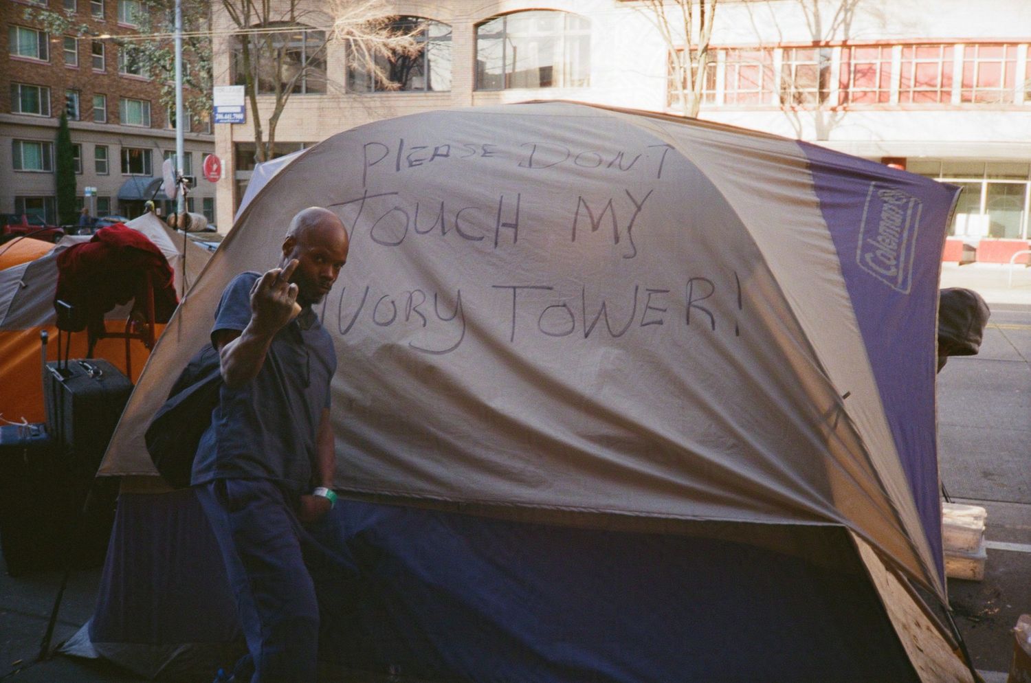 Unhoused man poses for photo outside street tent that reads 