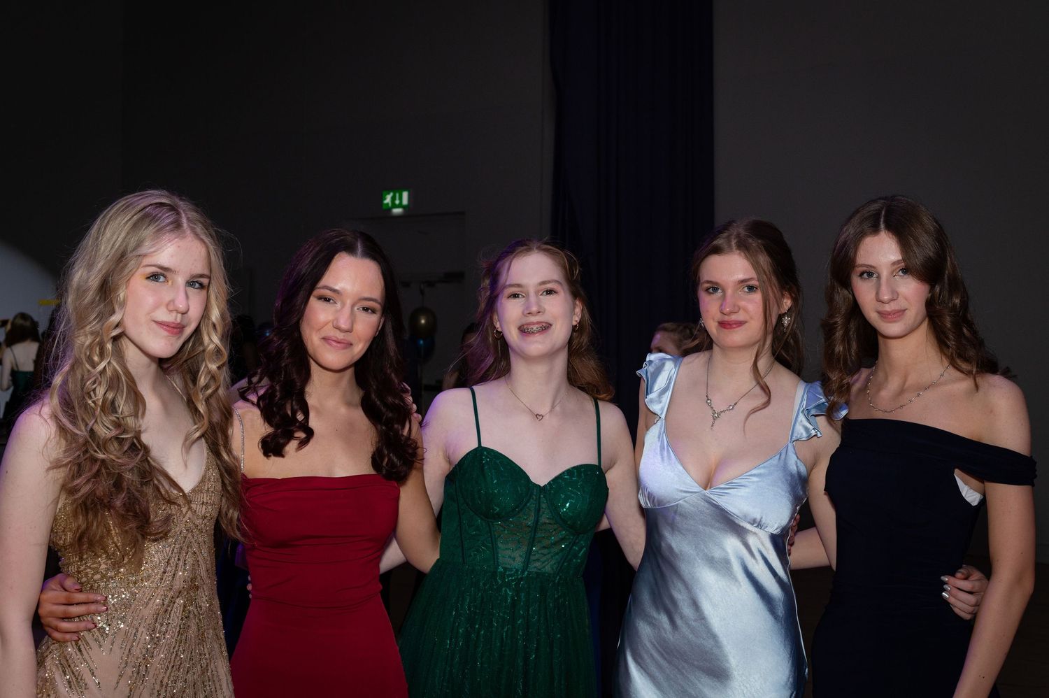 Girls posing with their friends for the camera at a winter ball party event in the hall of a school in Edinburgh in colour.