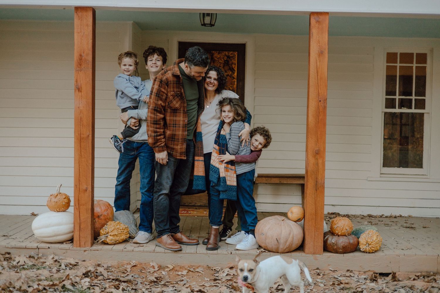 A family poses together on a porch decorated with pumpkins during autumn.