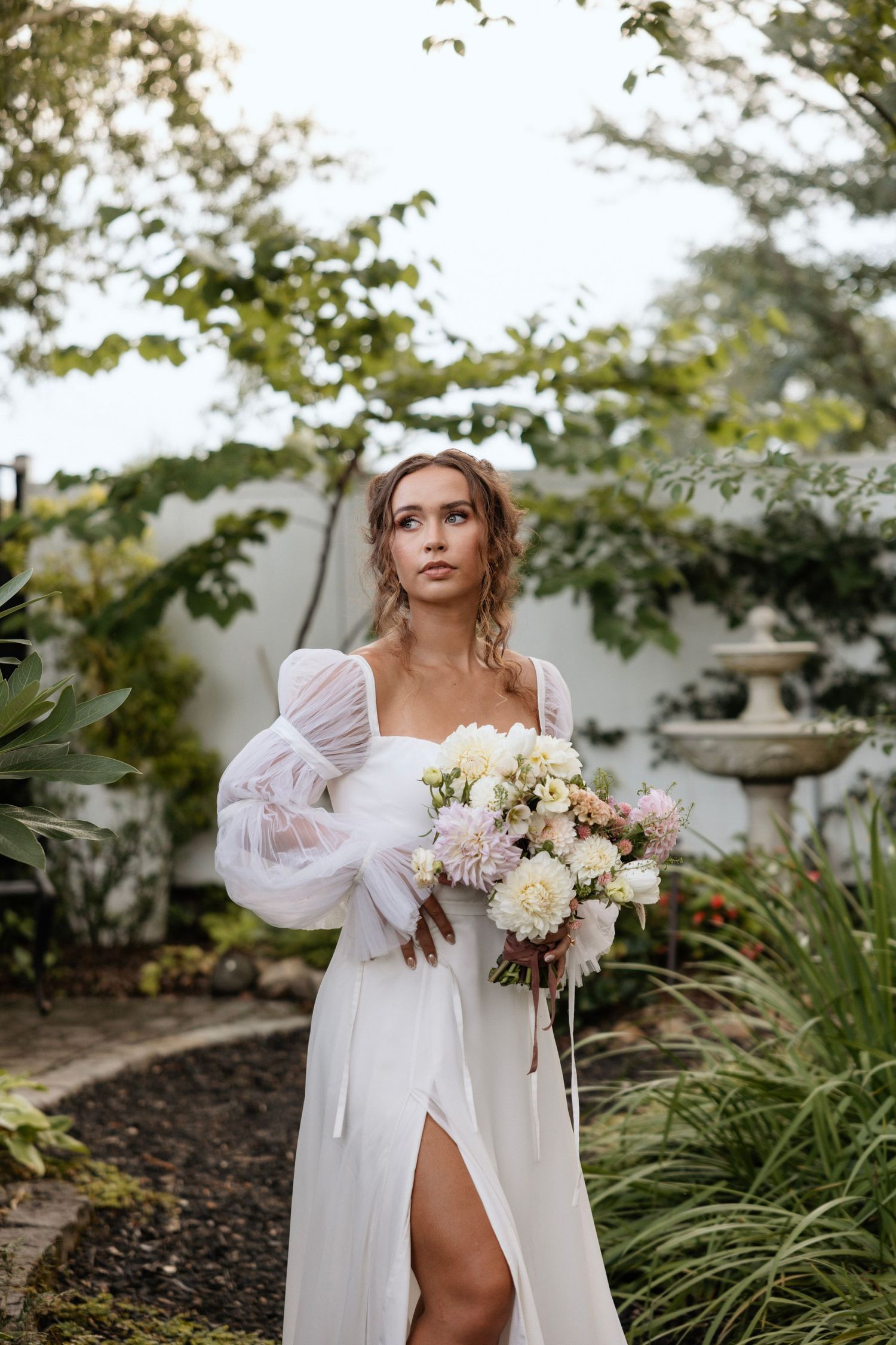 Ethereal bridal portrait in garden setting with flowing white dress and romantic bouquet.