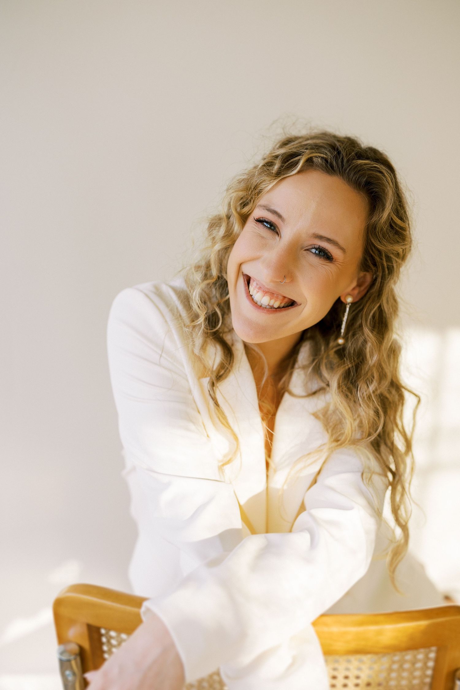 A joyful portrait in natural light showing someone with long curly blonde hair wearing a white top.