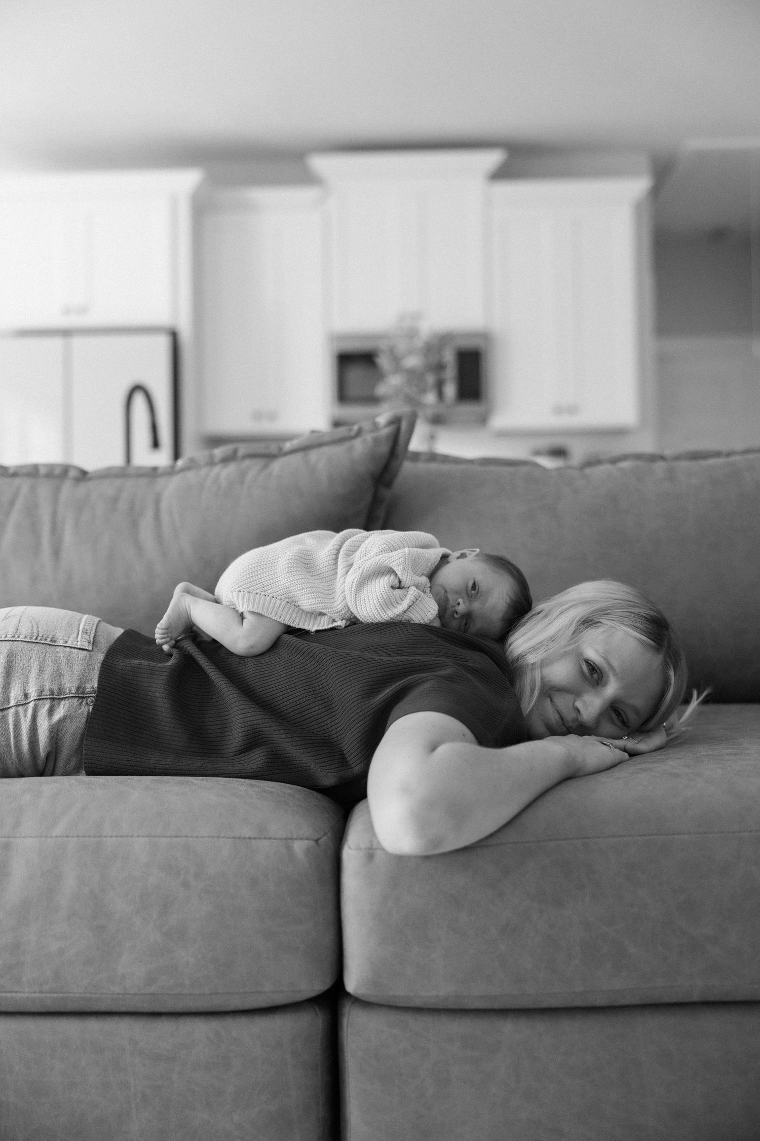 Black and white photo of a mother lying on a couch with her newborn baby resting on her chest.