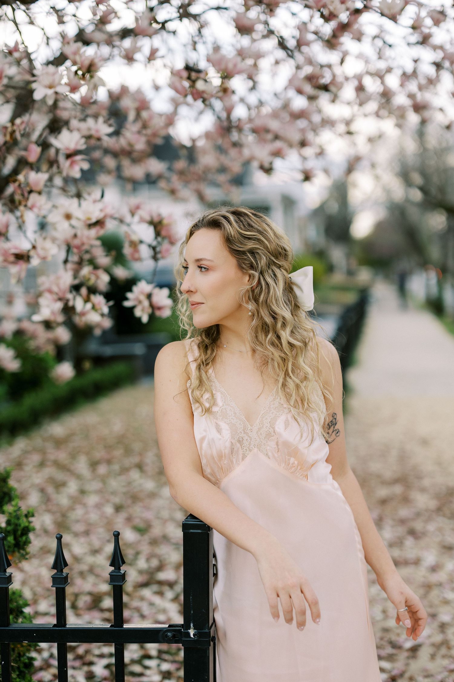 Springtime portrait with blooming cherry blossoms and a pink dress against an iron fence.