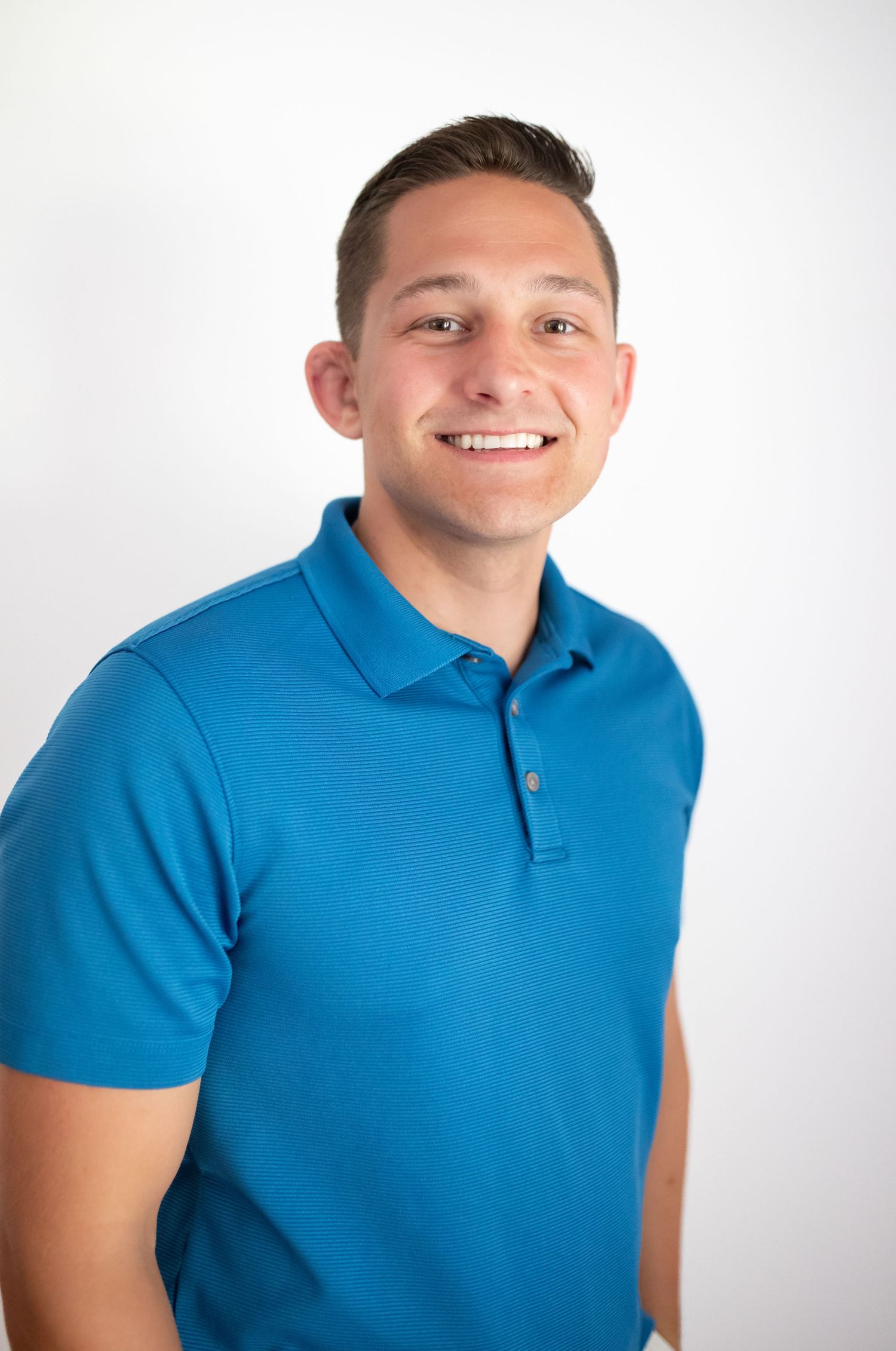 Professional headshot of man smiling in blue shirt with white background.