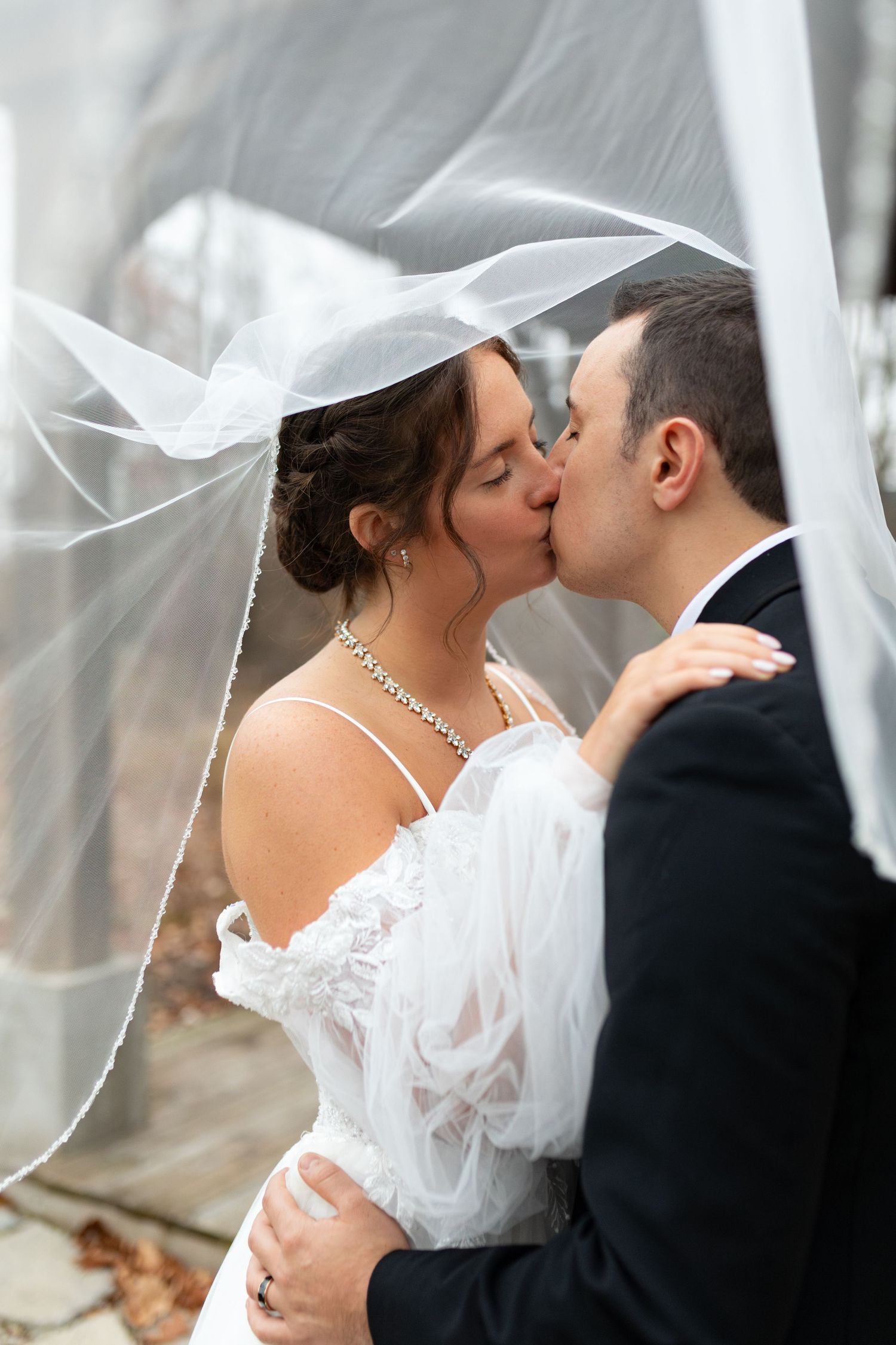 Elegant couple kissing under veil in wedding attire.