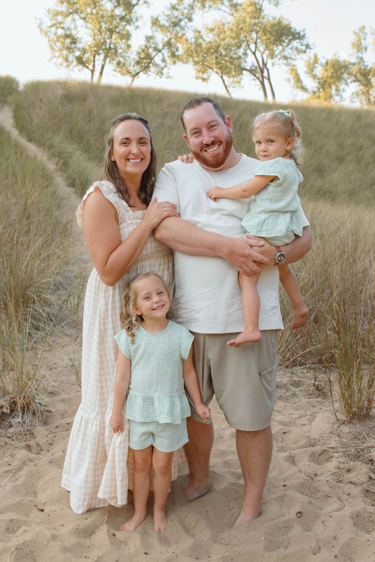 Parents with two young girls in matching outfits taking a family photo in the beautiful dune grass near the beach.