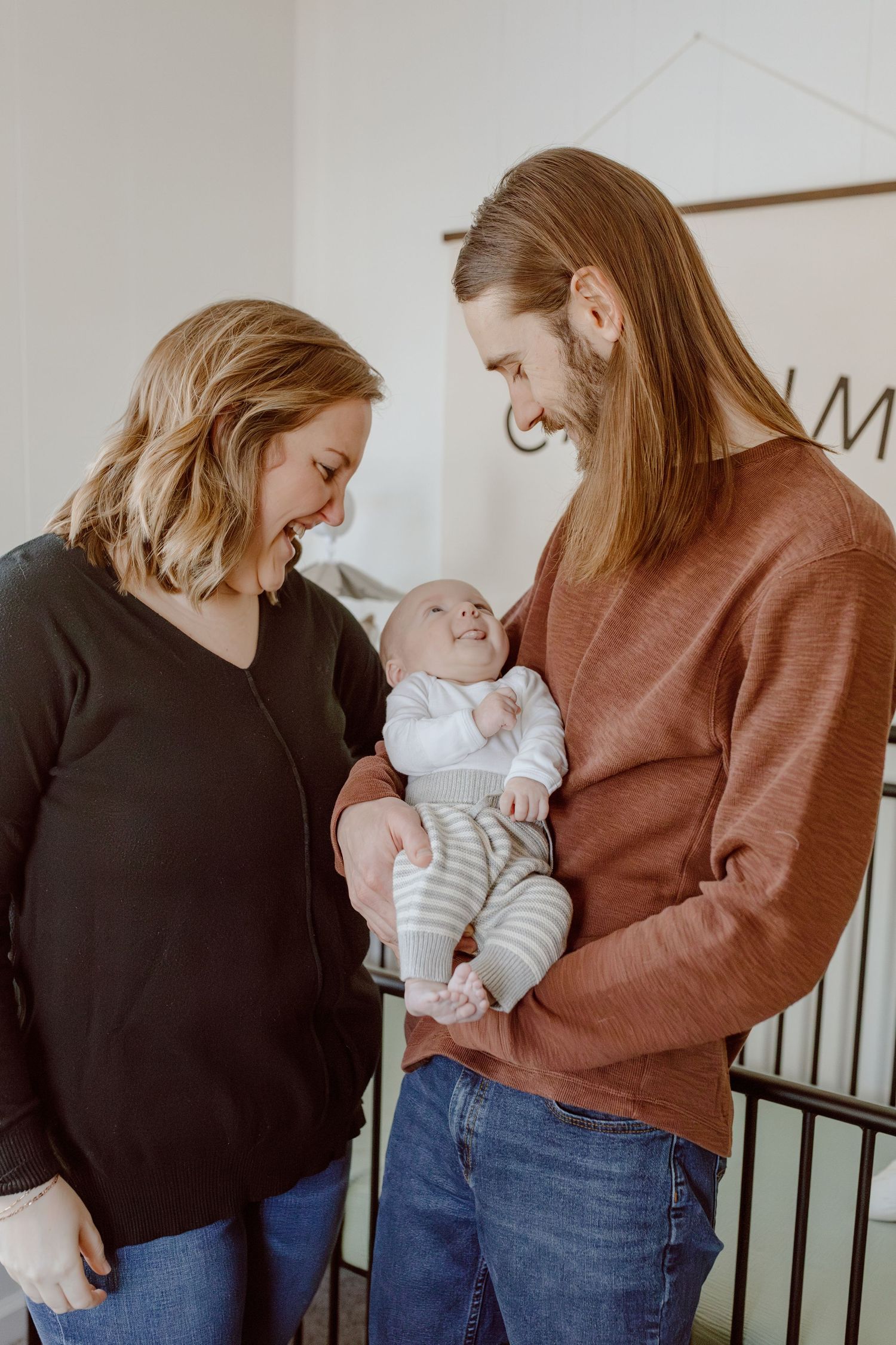 Couple smiling down at their newborn baby in their nursery during a newborn lifestyle photoshoot.