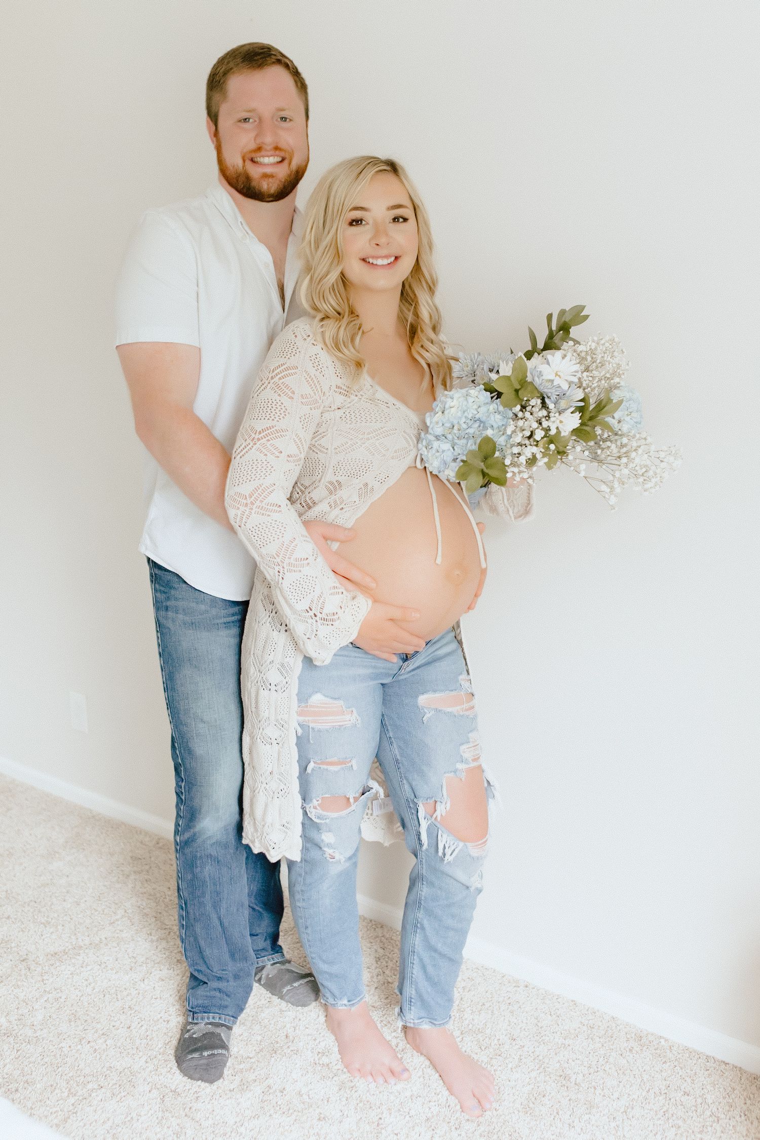 Couple posing in maternity photo in a studio styled photoshoot with floral arrangement.