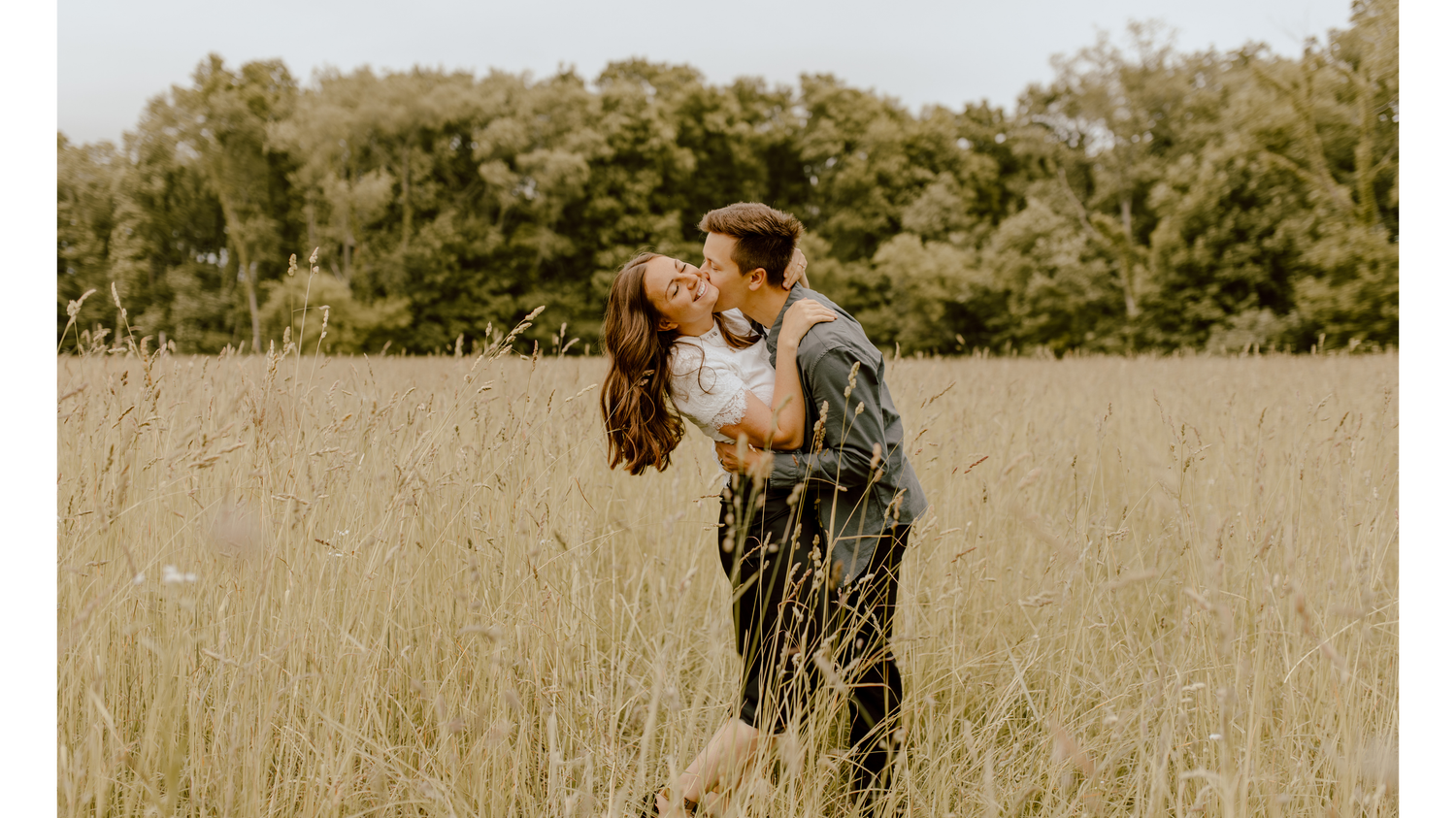 Husband dipping and kissing wife in golden hayfield surrounded y natural scenery.