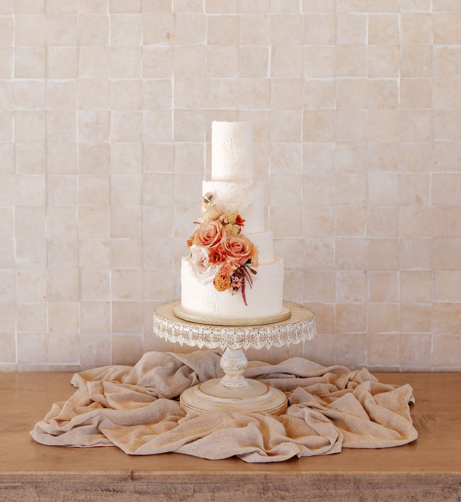 Elegant three-tier white wedding cake with peach floral accents on crystal stand.