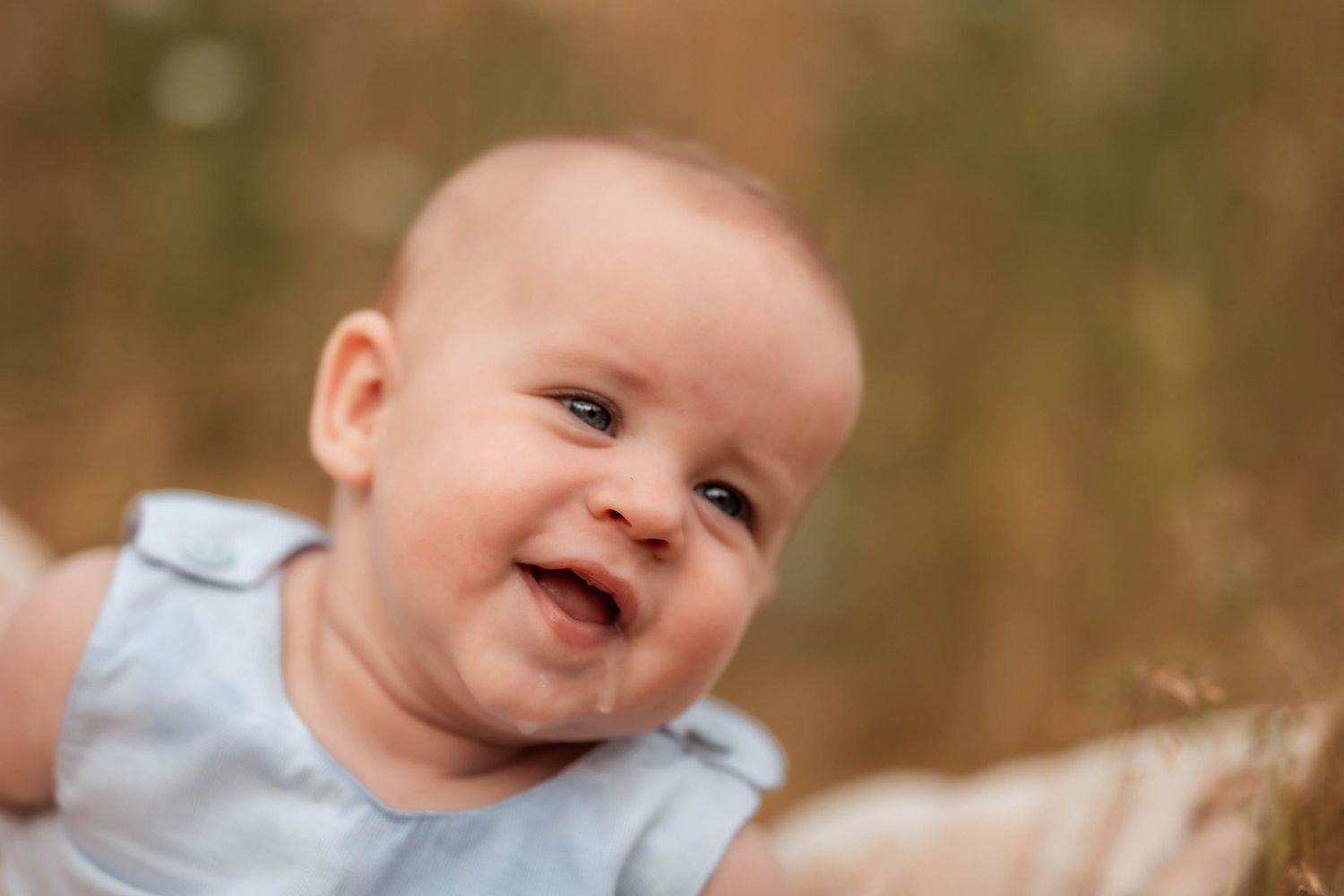 Smiling baby in a light blue outfit lying on a soft surface with a warm bokeh background.