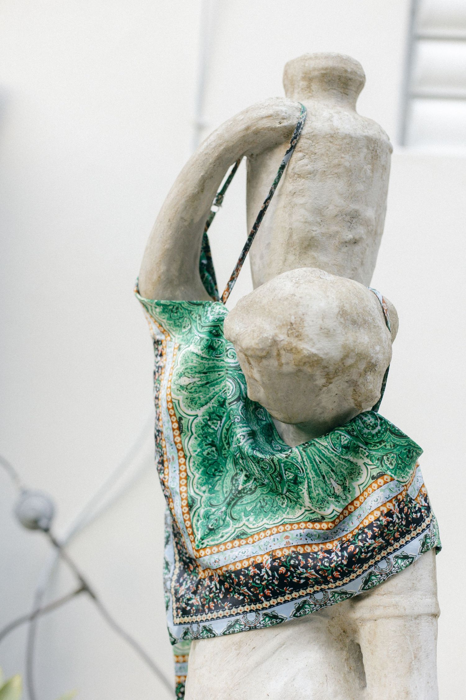 Stone statue wearing a decorative green and gold patterned fabric bag, viewed from behind against a white background.
