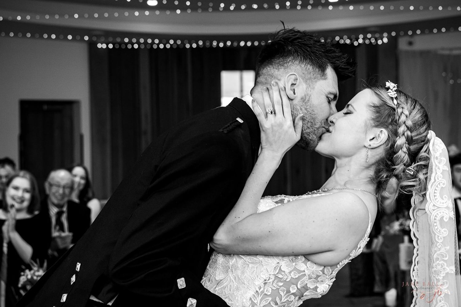 A couple shares their first dance at a wedding reception under twinkling string lights while guests watch from the sidelines.