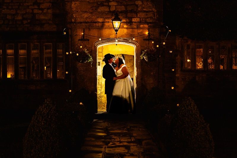 A romantic silhouette of newlyweds embracing in a warmly lit stone doorway at night with twinkling lights.